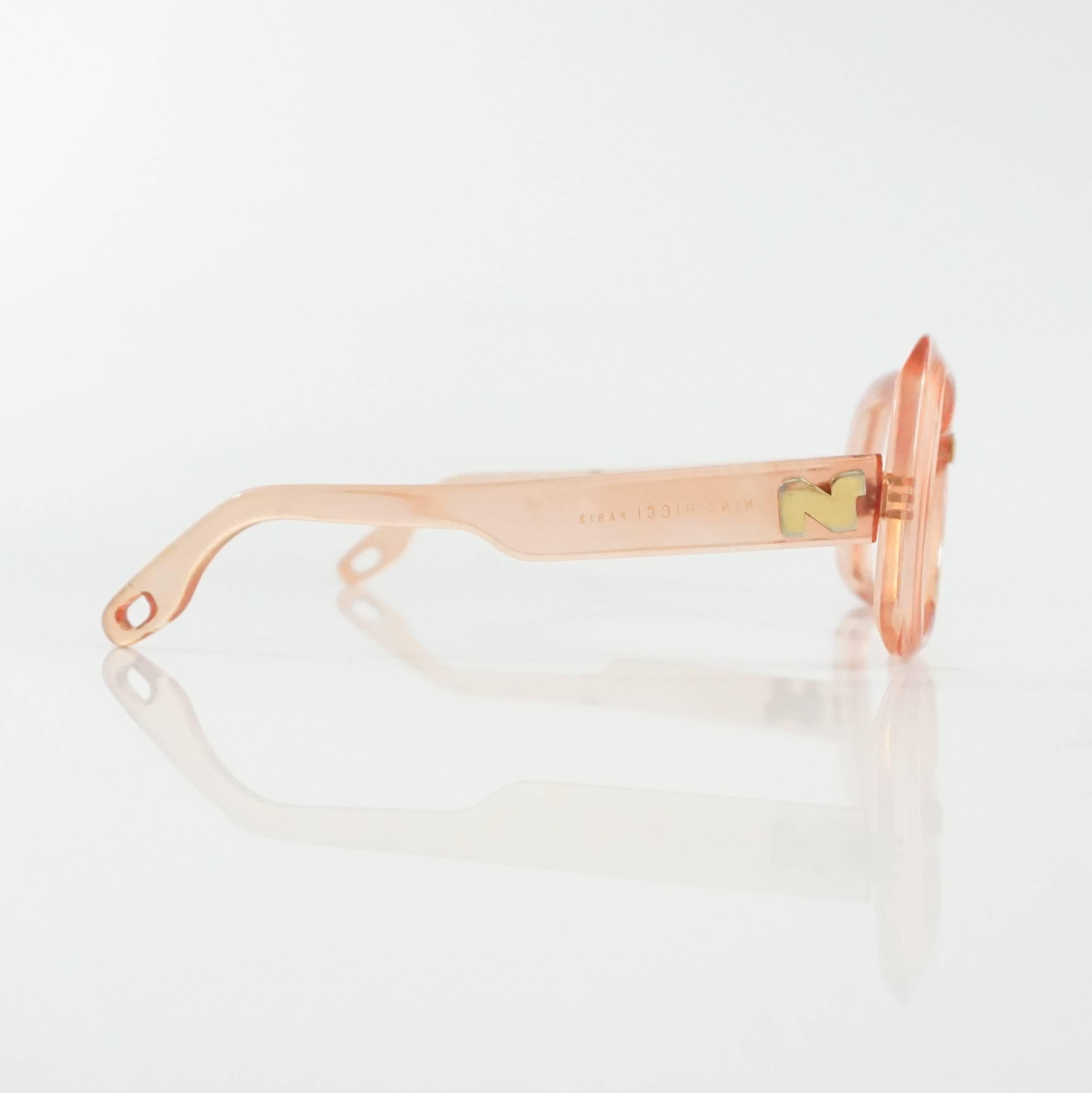 This vintage Nina Ricci sunglasses are made of pink Lucite. They feature square frames that do not have lenses and holes at the end of the legs to connect with a strap. They are in good vintage condition with some discoloration on the two side