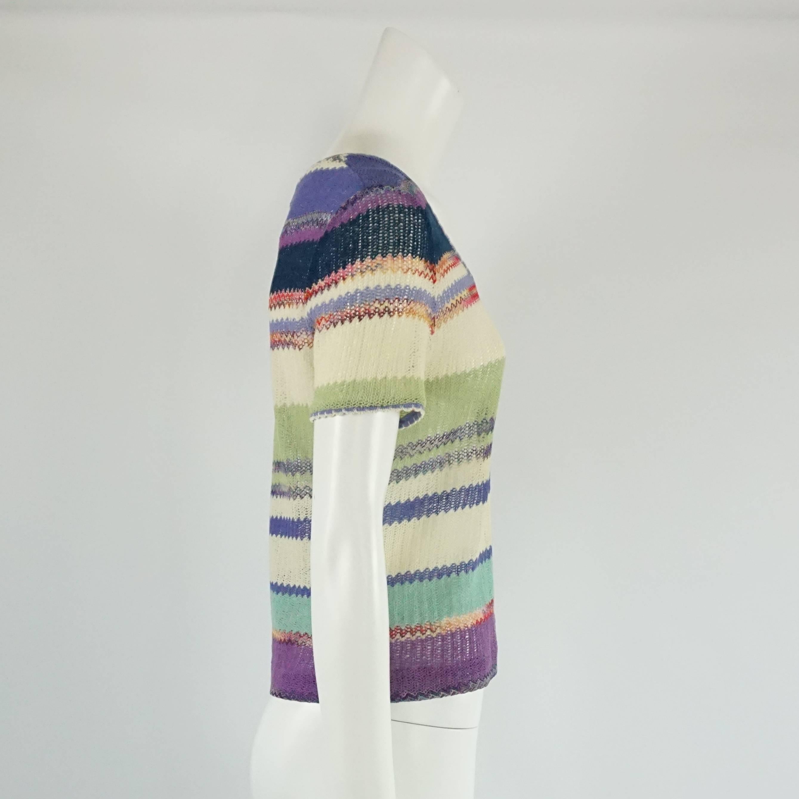This Missoni knitted top has a variety of colors including ivory, green, blues, purples, and red. The top is short sleeved with a round neck and sheer fabric. The piece is in good condition with minimal general wear and a couple small blemishes to