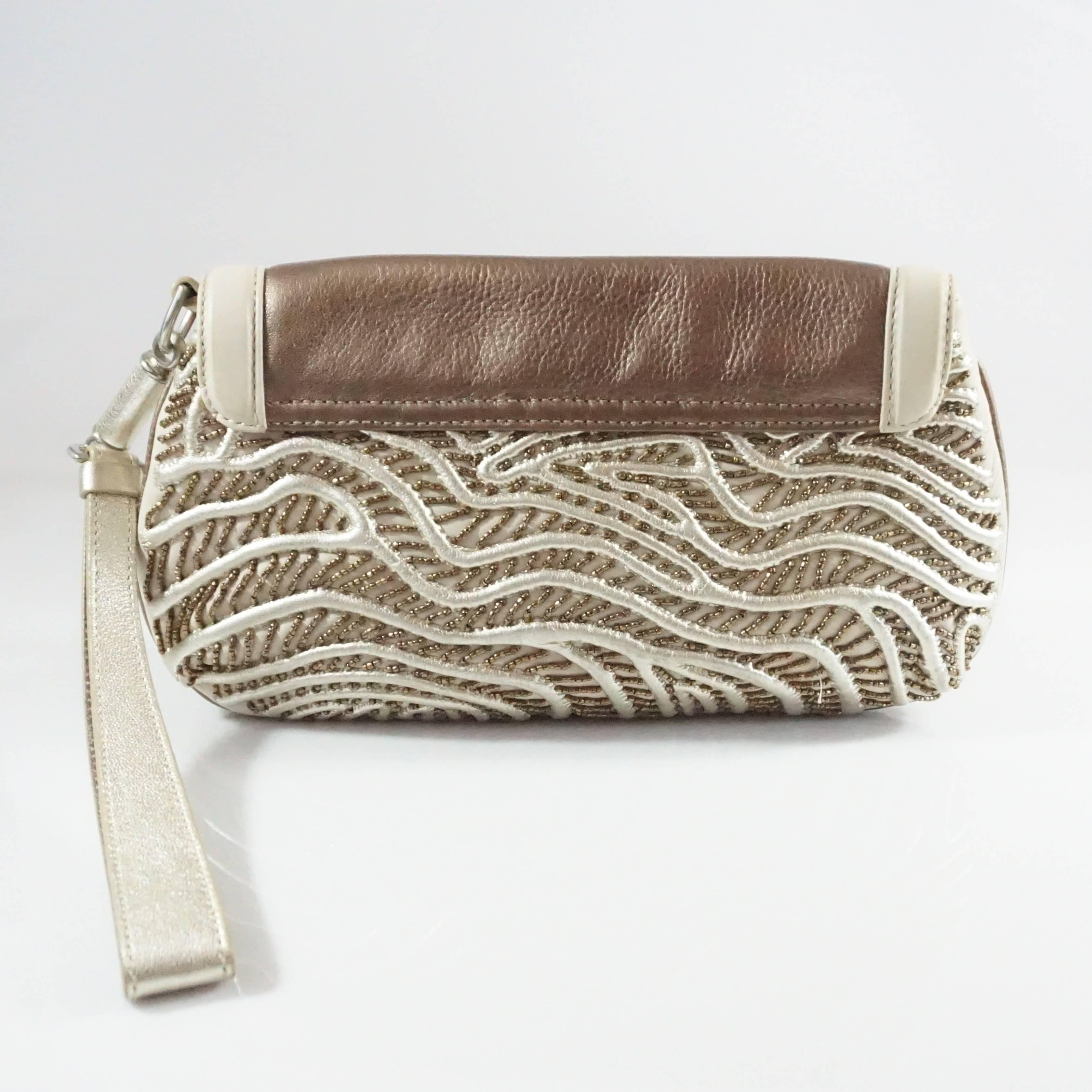 This Alberta Ferretti clutch is a roomy statement clutch. It's made of ivory leather with gold ribbing and brown bead detailing and also has a bronze leather flap. Additionally, the bag features a snap clasp, horn detail, wrist strap, and 1 interior