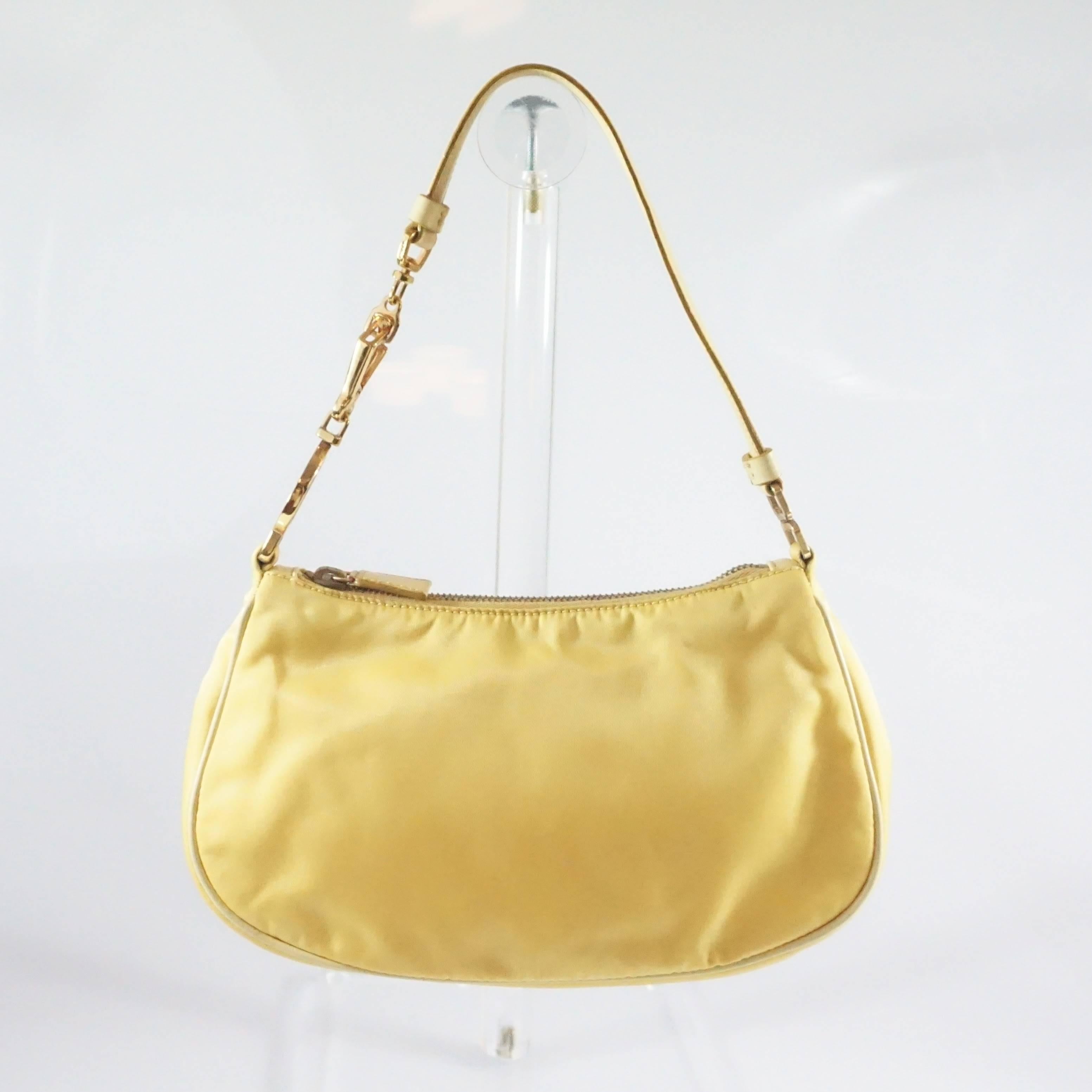 This Prada yellow baguette is made of nylon and has leather accents. The bag features the signature Prada enamel logo and a removable leather strap with gold hardware accents. The bag is in good condition with some hardware tarnishing and wear to