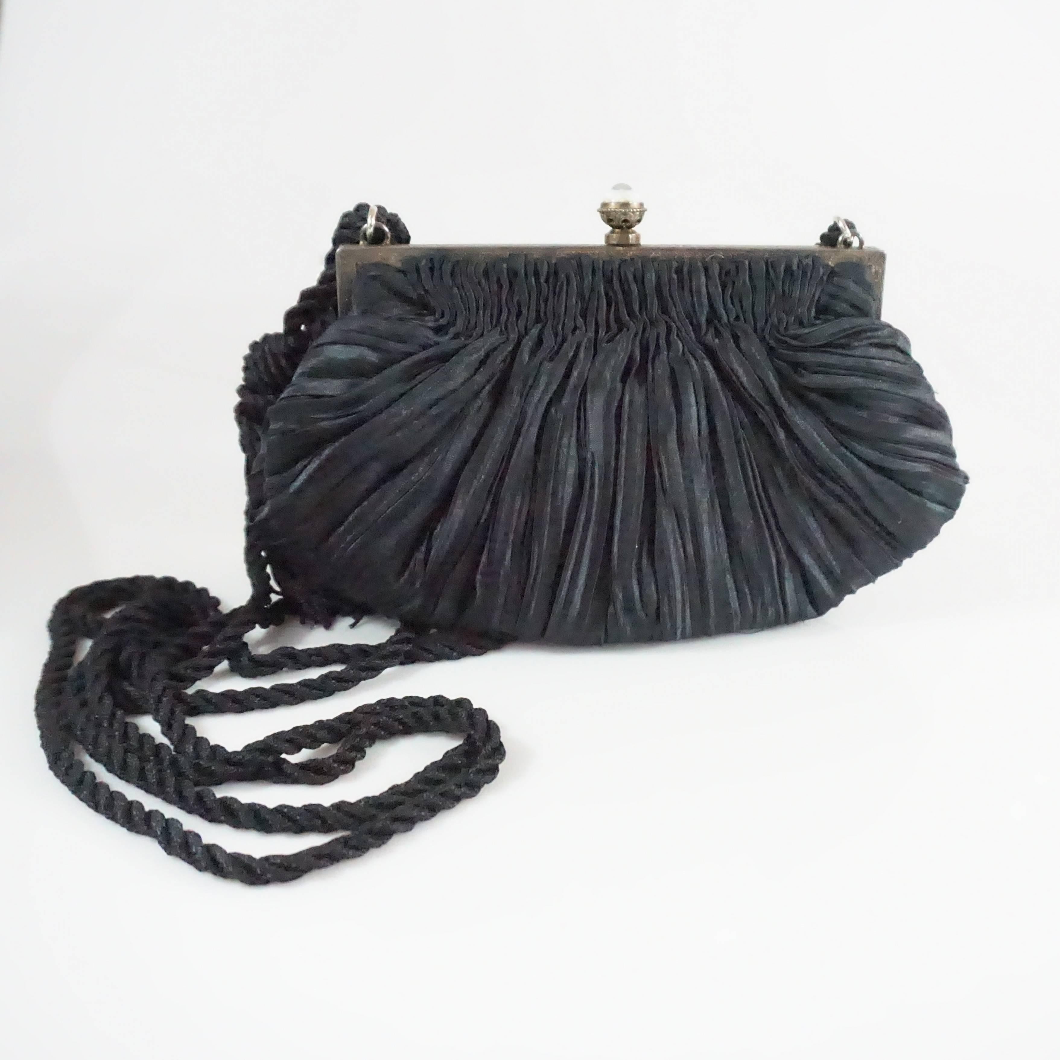 This Revivals bag is made of a black plated satin fabric. The frame of the piece also has etching with an ivory and red enamel design and small graphite stones. The bag also features a push clasp, 1 small interior pocket, and a rope strap with