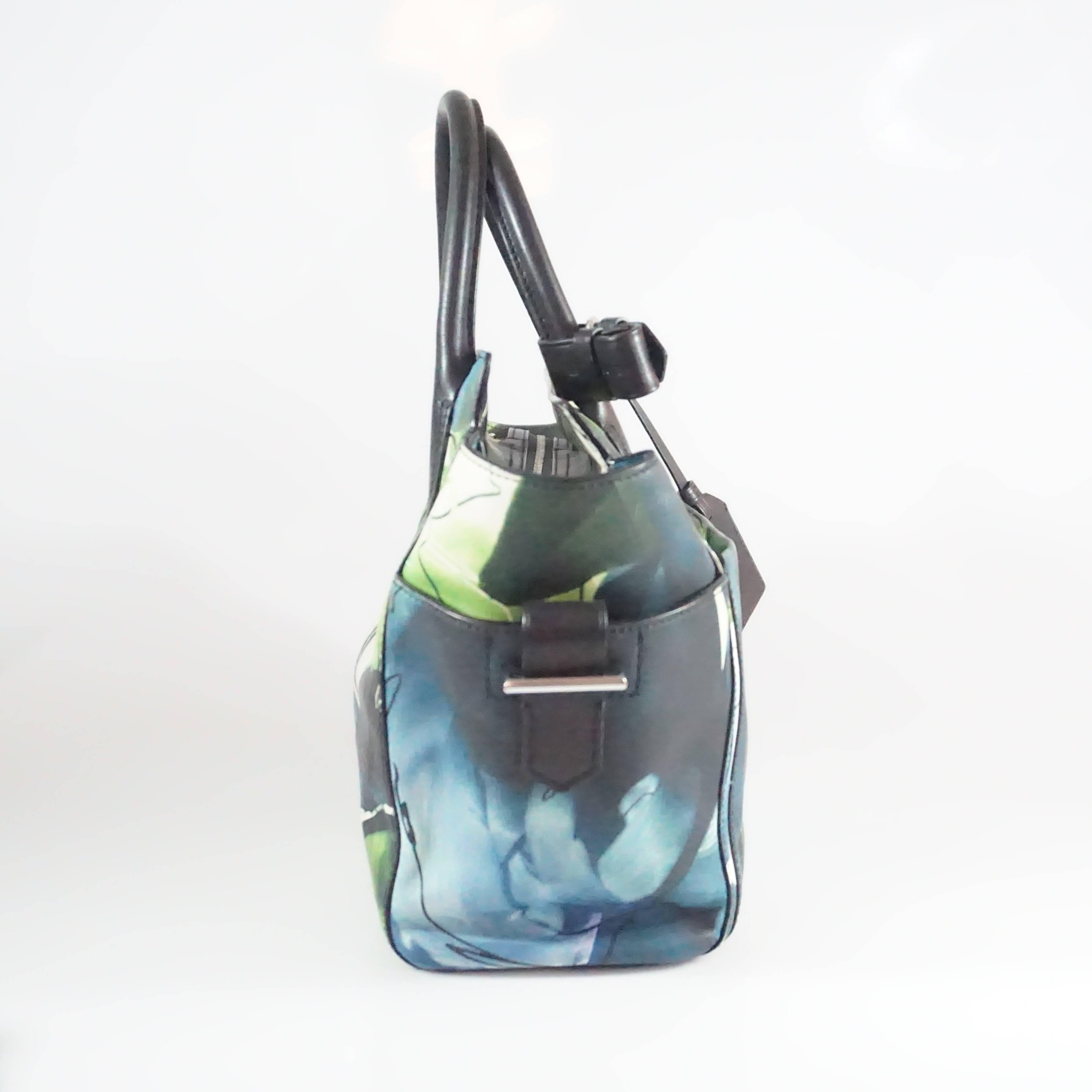 This Reed Krakoff leather mini tote has a print with hues of blue, green, black, and white. The bag features side flaps, 3 outer pockets, a zip closure, and 1 interior zip pocket. The bag is in fair condition with some wear to the leather as