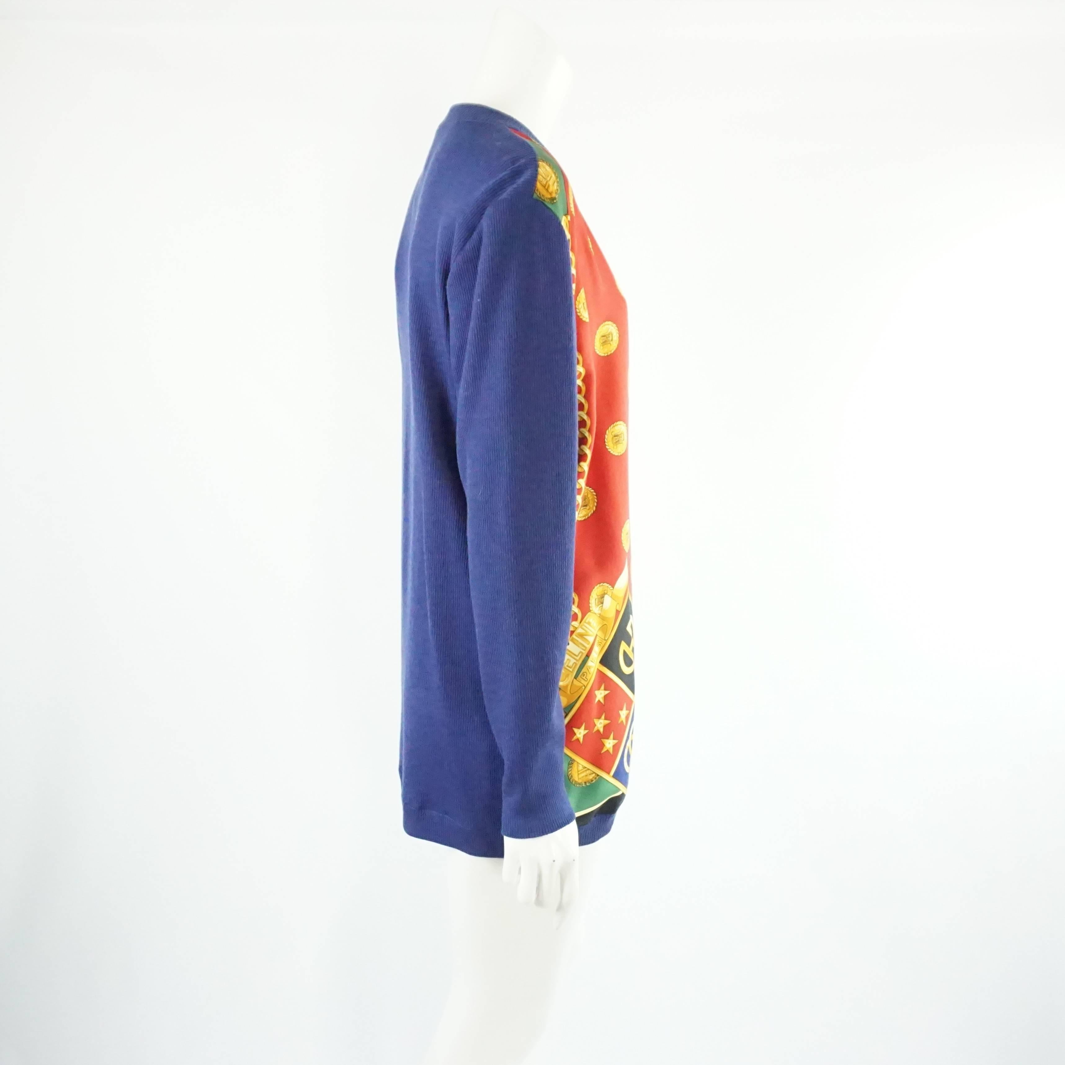 This gorgeous Celine cardigan is made of a blue knit material with a multi-color printed silk front. The print features regal accents such as a coat of arms, golden chains, and coins. The piece is in excellent vintage condition with minimal wear.