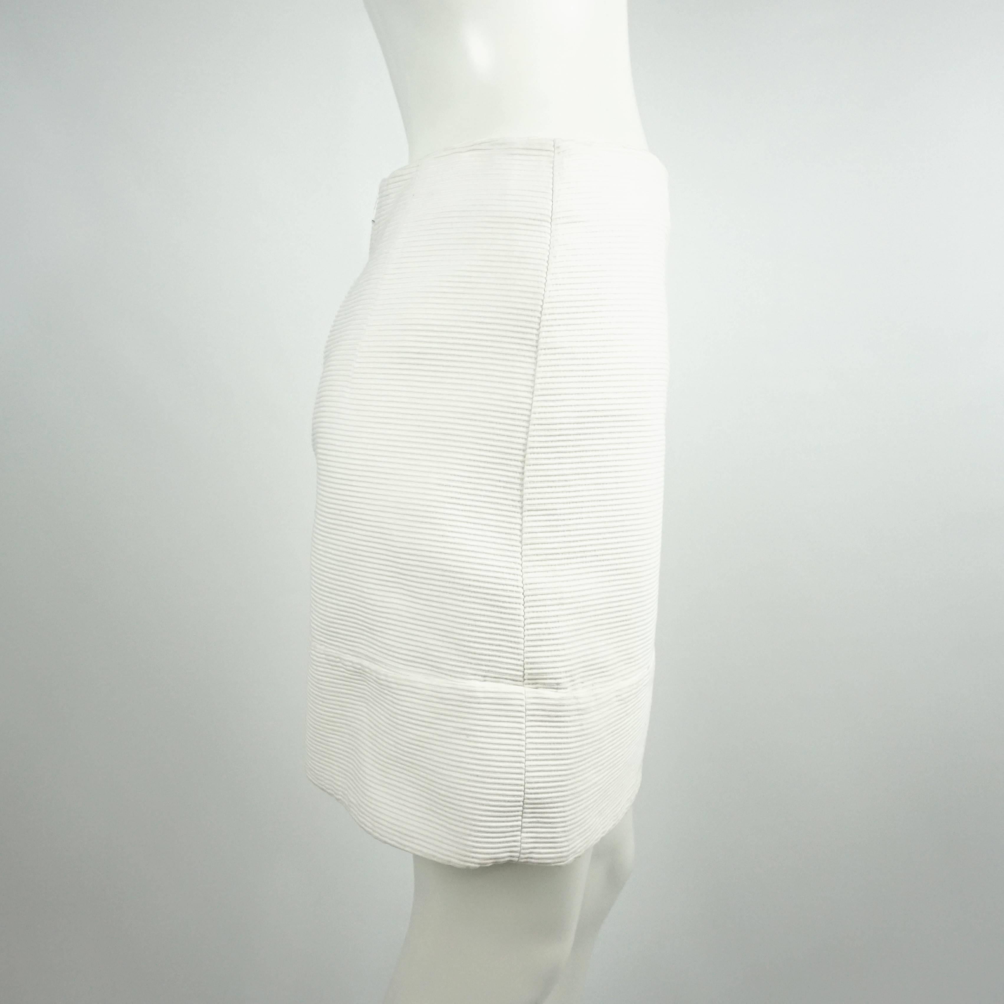 This Chloe white ribbed cotton skirt is fully lined in silk and has a straight cut. The fabric is ribbed and has a bottom section creating the illusion of a trim. The skirt also zips in the back with a "Chloe" logo white zipper. The piece