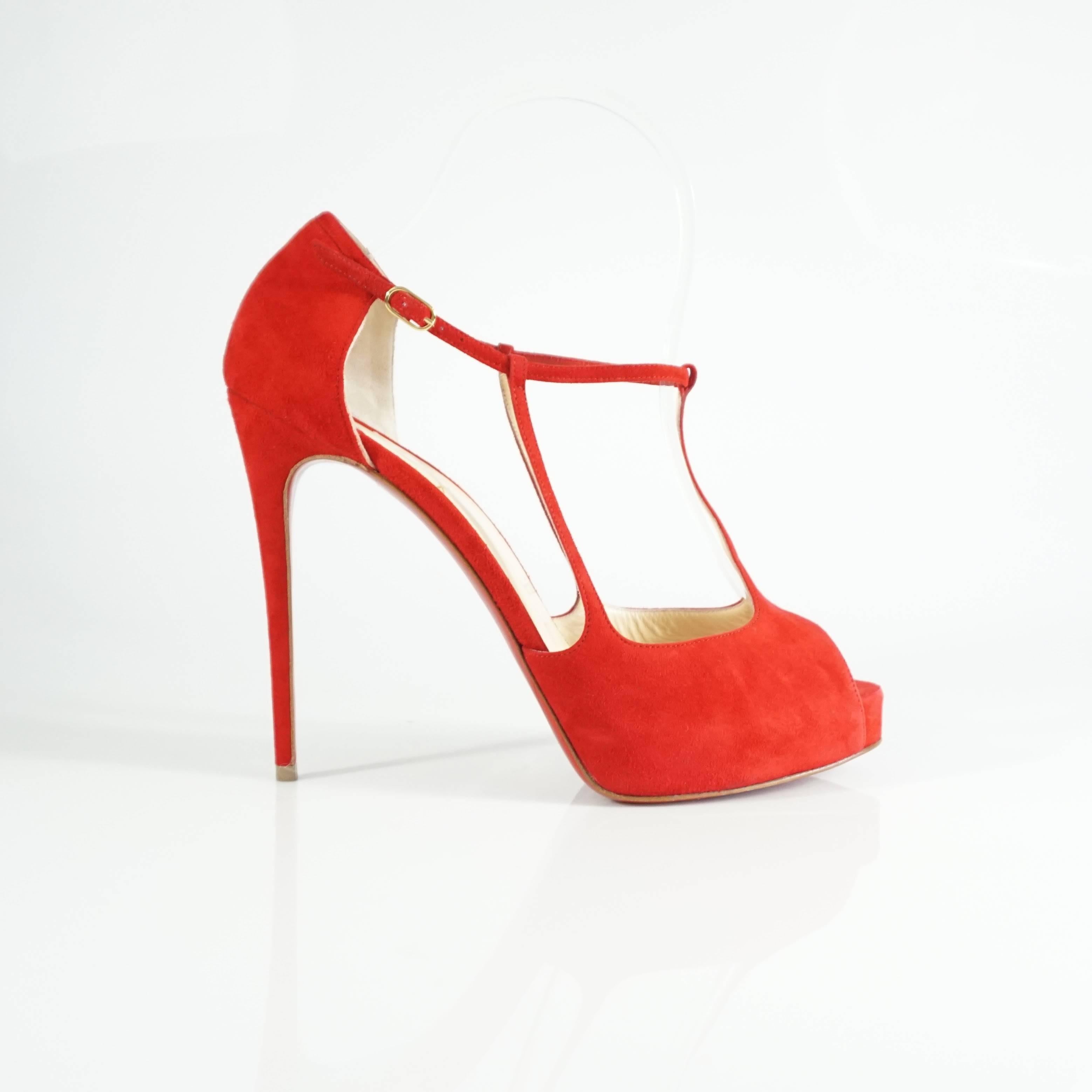 These Christian Louboutin heels are made of red suede. They are t-strap style with an additional strap on each side, a platform, and a stiletto heel. The shoes are in very good condition with minimal fabric wear, one area on the inside near the