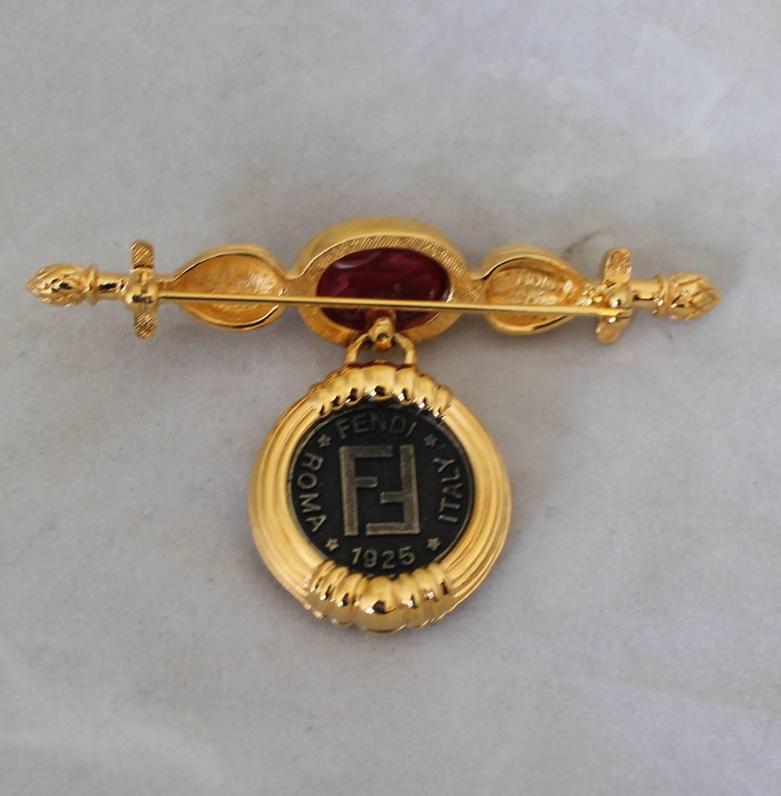 1980's Vintage Fendi Cabochon & Double Janis Head Coin Goldtone Pin. This pin is in excellent vintage condition.

Height- 1.75"
Width- 3"