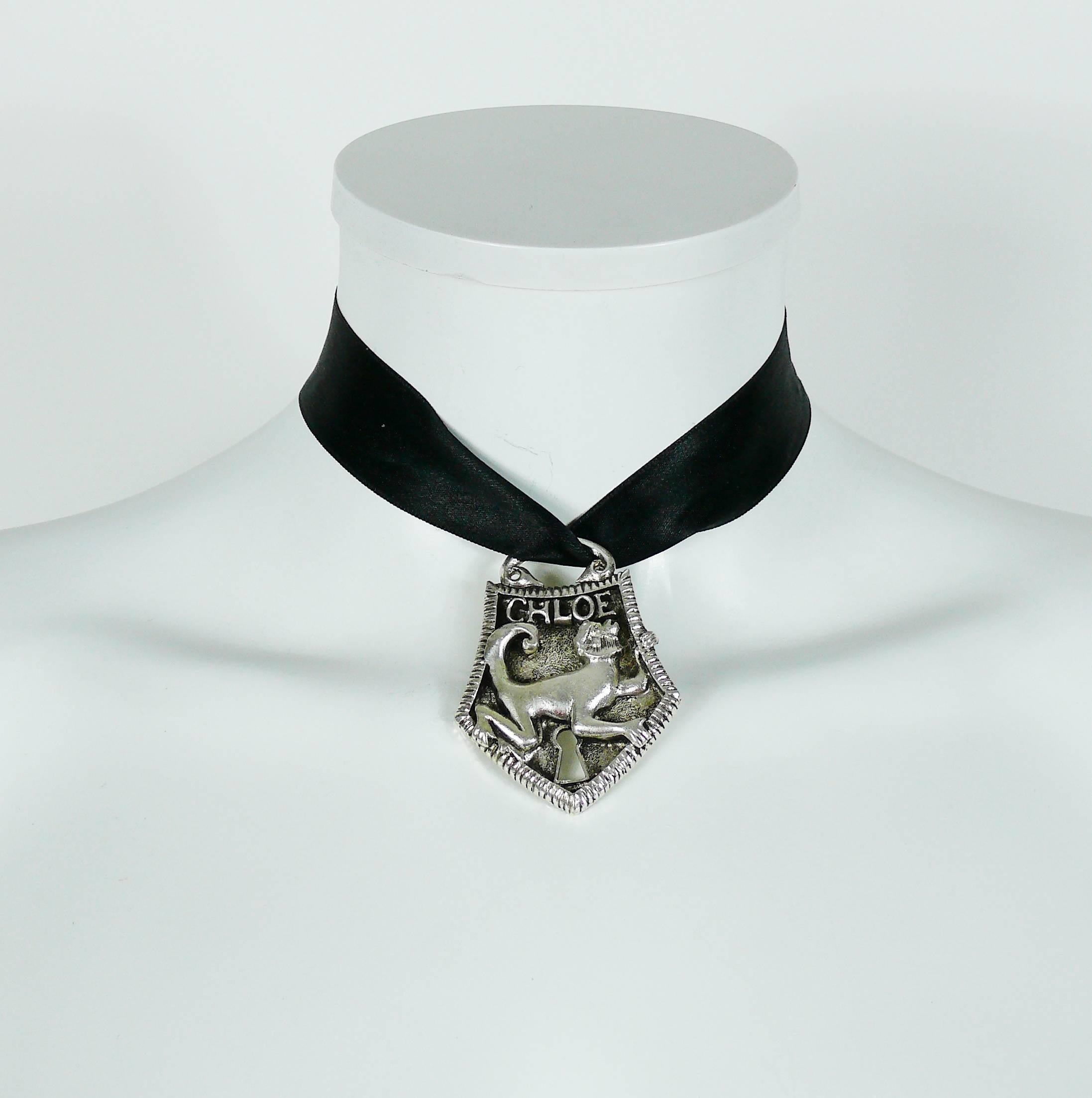 Collana con ciondolo in tonalità argento anticato di CHLOE con chiusura a scimmia.

Nastro di raso nero.

CHLOE in rilievo.

Misure indicative: lunghezza del nastro circa 57 cm (22,44 pollici) / ciondolo circa 5,9 cm (2,32 pollici) x 4,5 cm (1,77