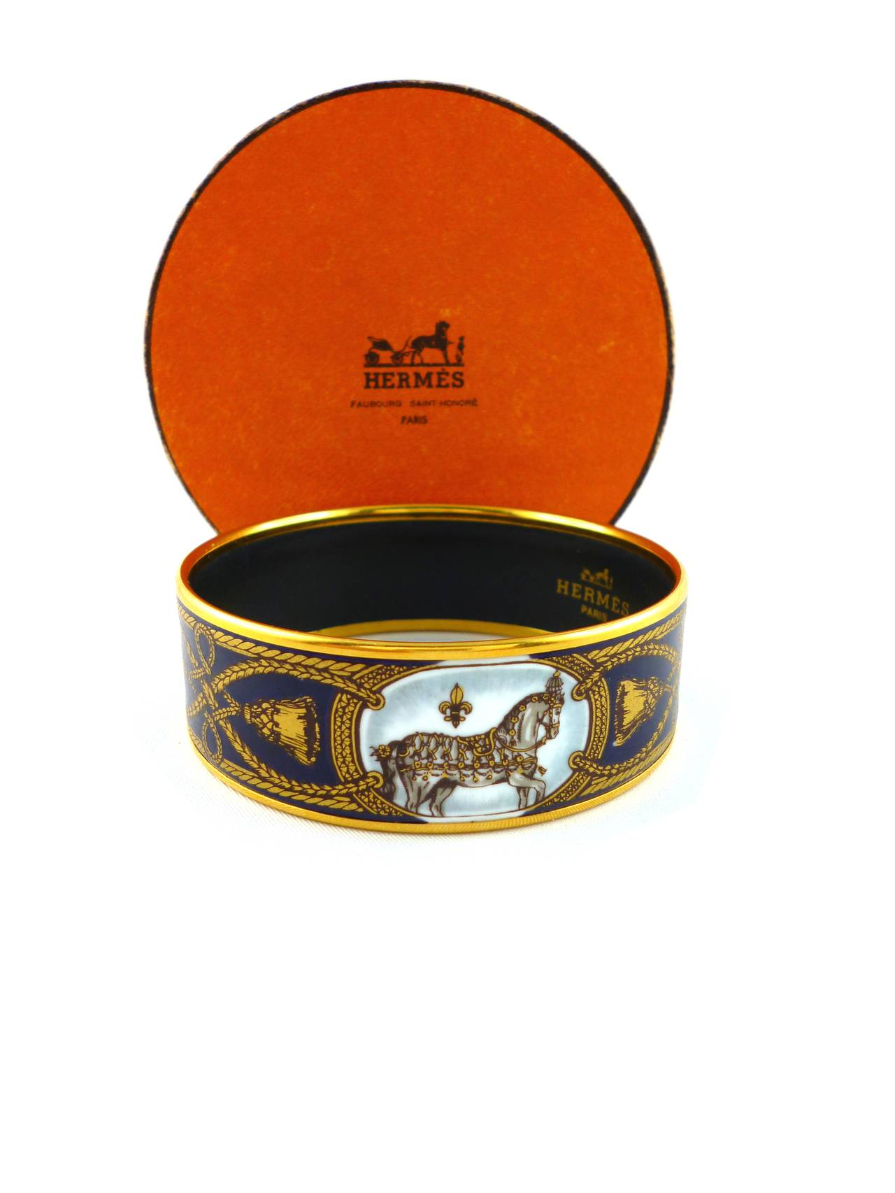 HERMES vintage Grand Apparat printed enamel wide cuff bracelet.

Printed enamel horses with gold tone brandebourg and tassel patterns on a deep blue background. Gold plated rim.

Size PM (65).

Marked HERMES Paris Made in Austria.
Stamped