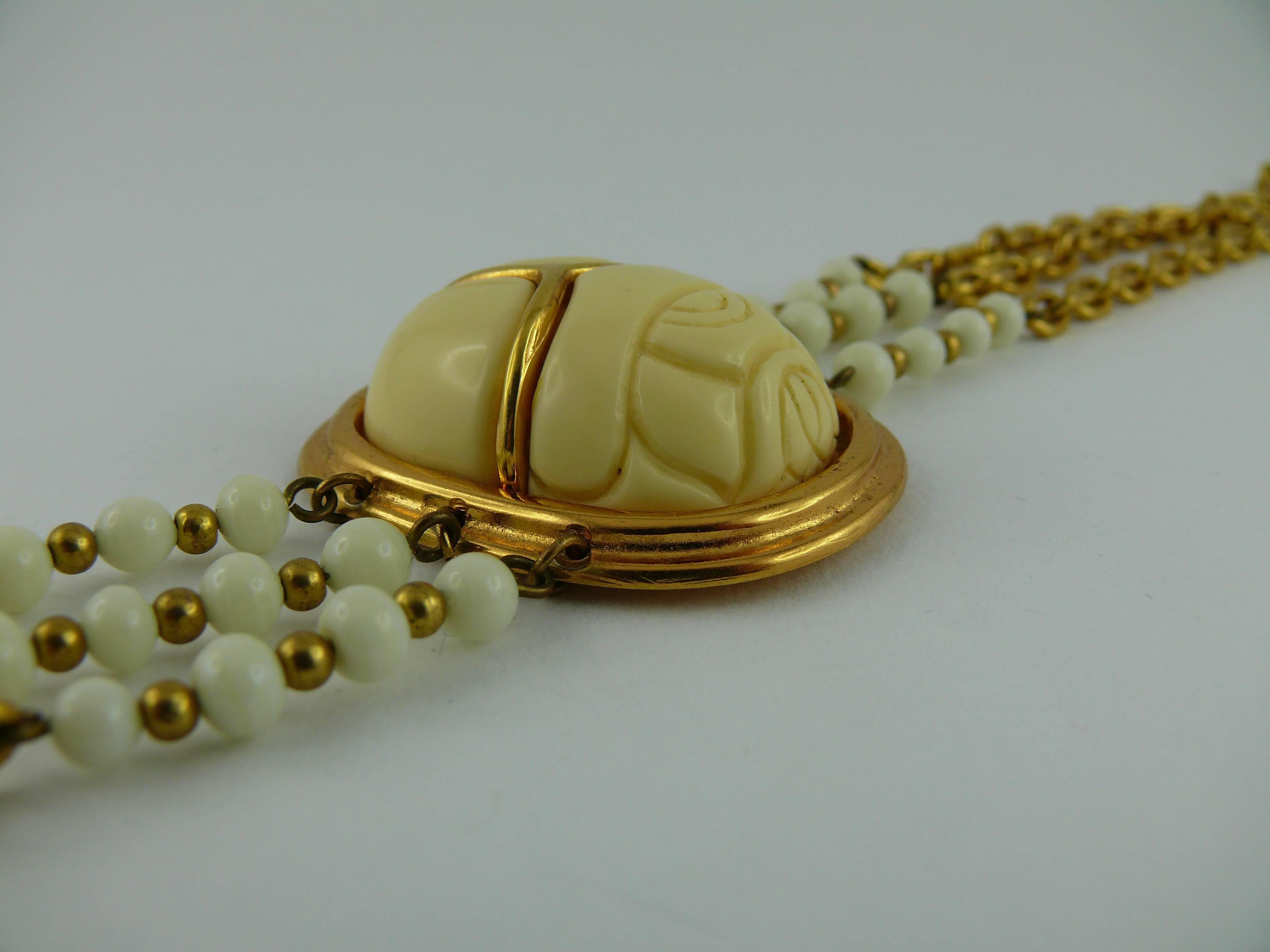 PIERRE BALMAIN vintage Egyptian revival scarab choker necklace.

This necklace consists of three raws of gold tone chain with white glass beads. Central oval medallion featuring a carved faux ivory scarab in a gold tone setting.

Embossed