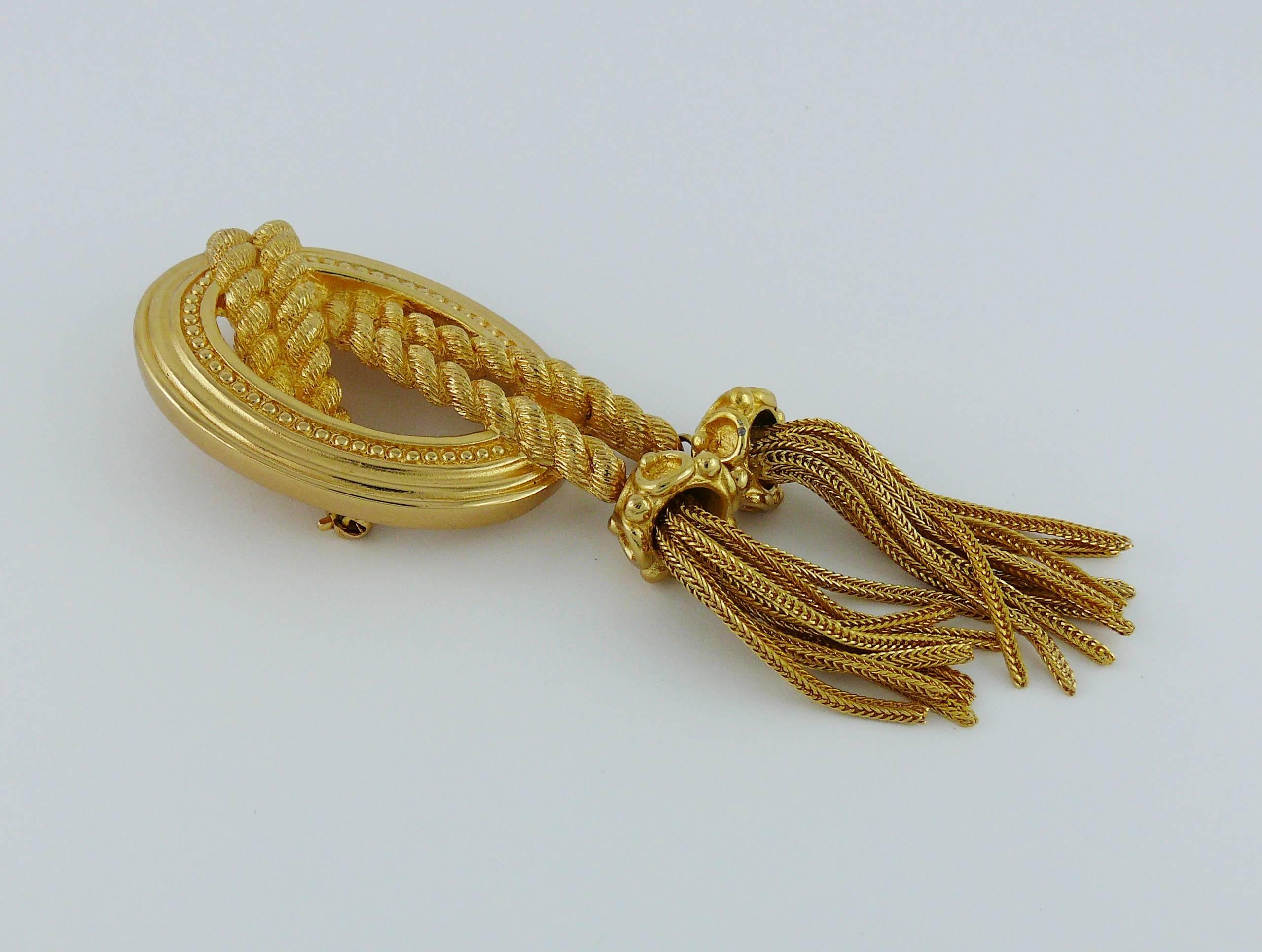 CHRISTIAN DIOR vintage gold tone booch featuring the iconic medallion of the House with tassels and intertwined rope.

Marked CHR. DIOR.

Indicative measurements : length approx. 9.5 cm (3.74 inches) / width approx. 3.2 cm (1.26 inches).

JEWELRY