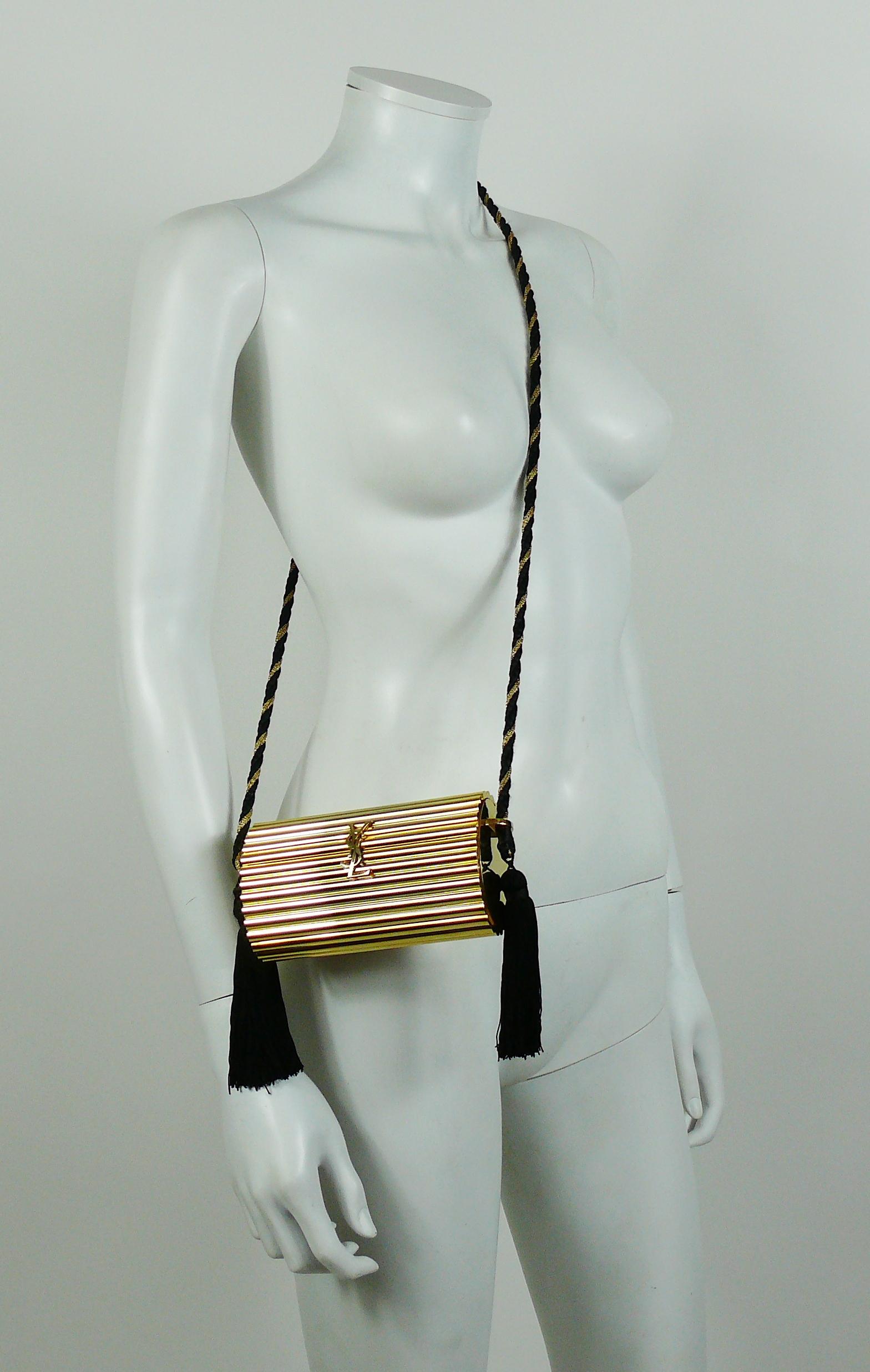 YVES SAINT LAURENT rare and collectable vintage gold tone ribbed minaudiere featuring :

- Hard box cylindric resin  body.
- Large YSL logo at the front.
- Black and gold braided shoulder strap.
- Long black tassels.
- Gold canvas