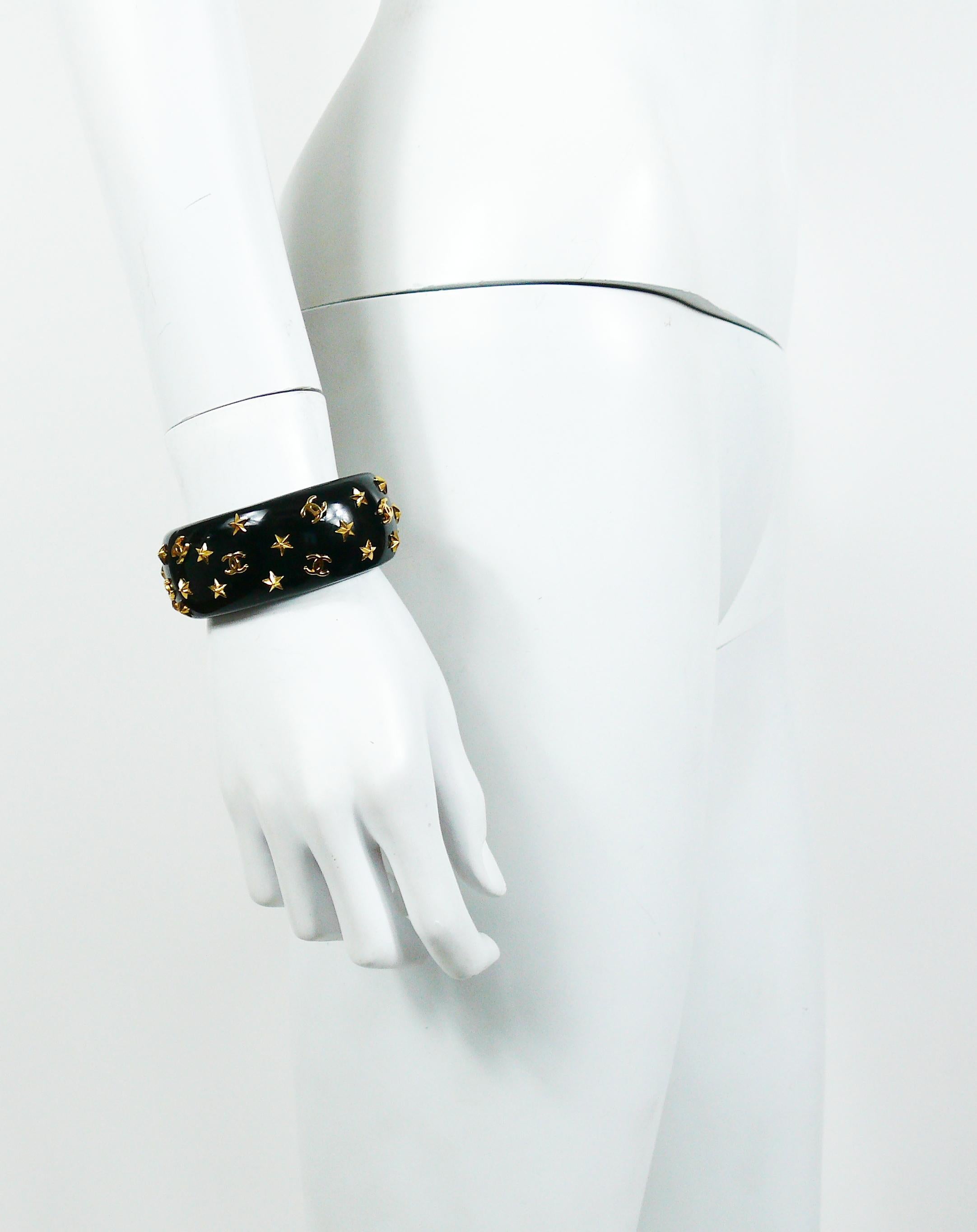 CHANEL vintage 1995 iconic black resin cuff bracelet featuring gold toned stars and CC logos. 

Fall/Winter Collection 1995.

Embossed CHANEL 95 A Made in France.

Indicative measurements : inner approx. 5.5 cm (2.17 inches) x 4.5 cm (1.77 inches) /