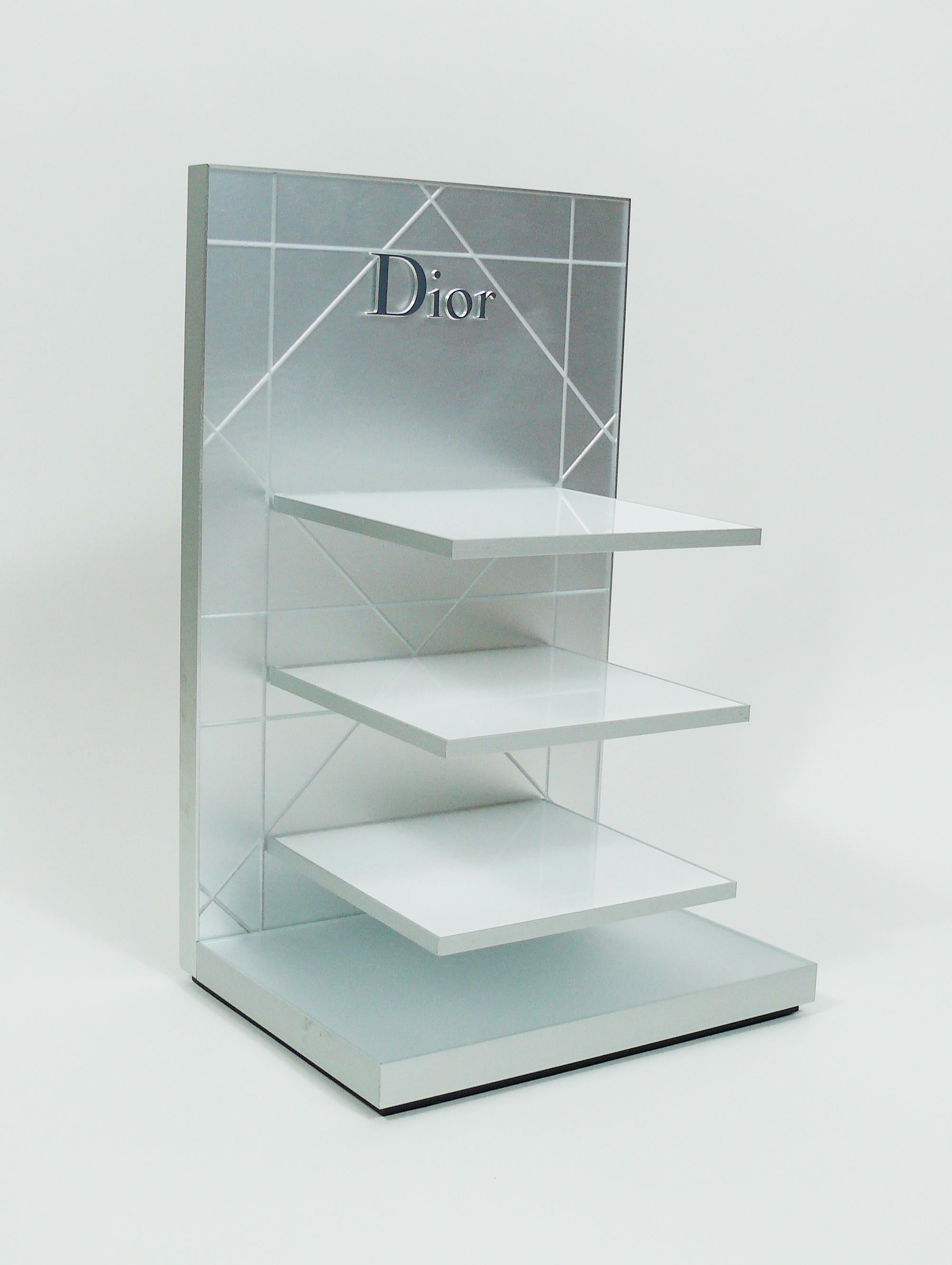 CHRSITIAN DIOR presentation pos display featuring :

- Quilted design in matte frosted PVC background.
- DIOR logo on each side (grey color at front, silver color on reverse).
- Three white plexiglass shelves.
- Silver coloured metal frames.
- Black