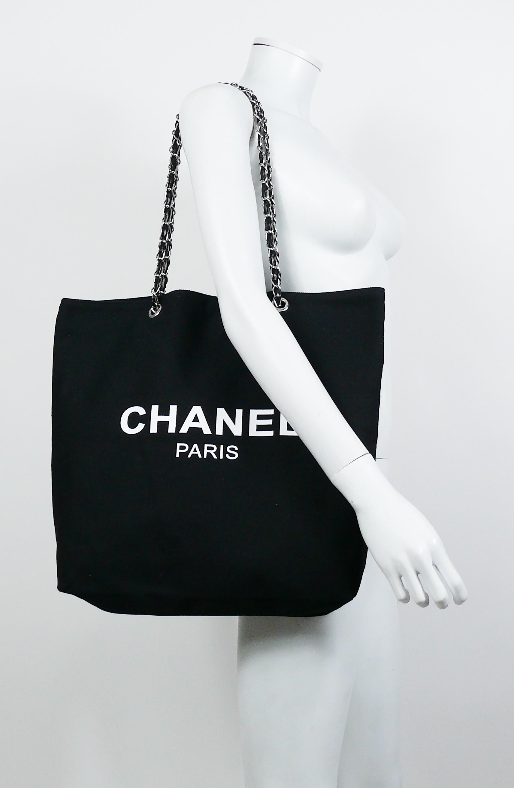 CHANEL black canvas tote shopping promotional gift bag.

This bag features :
- Black canvas body.
- White flocked CHANEL PARIS on one both sides.
- Silver toned chains with intertwined black faux leather (PVC) straps.
- Magnetic closure.
- Silver