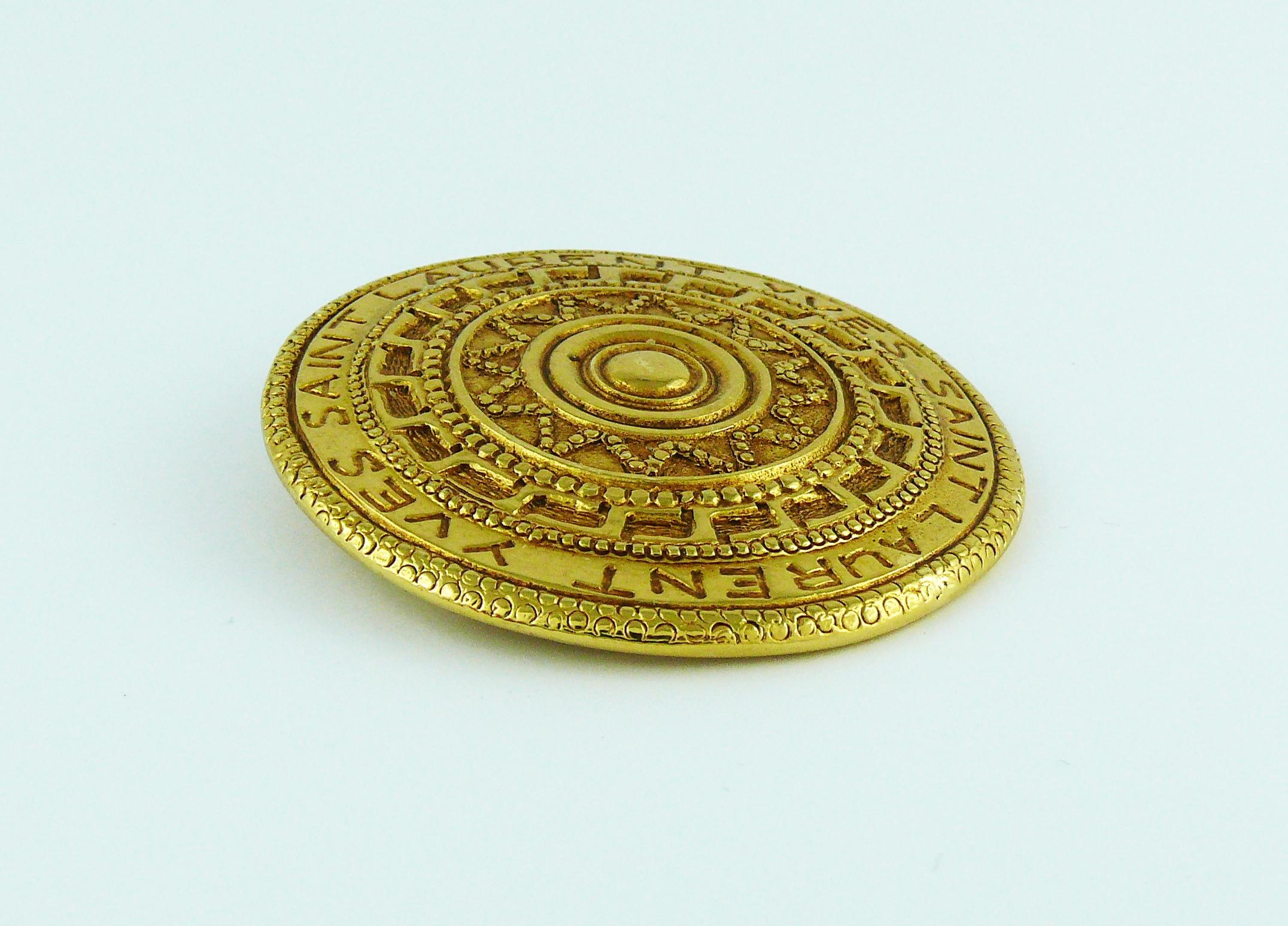 YVES SAINT LAURENT vintage gold toned shield brooch featuring ethnic Aztec pattern engraved YVES SAINT LAURENT.

Embossed YSL.
Made in France.

Indicative measurements : diameter approx. 5.4 cm (2.13 inches).

JEWELRY CONDITION CHART
- New or never