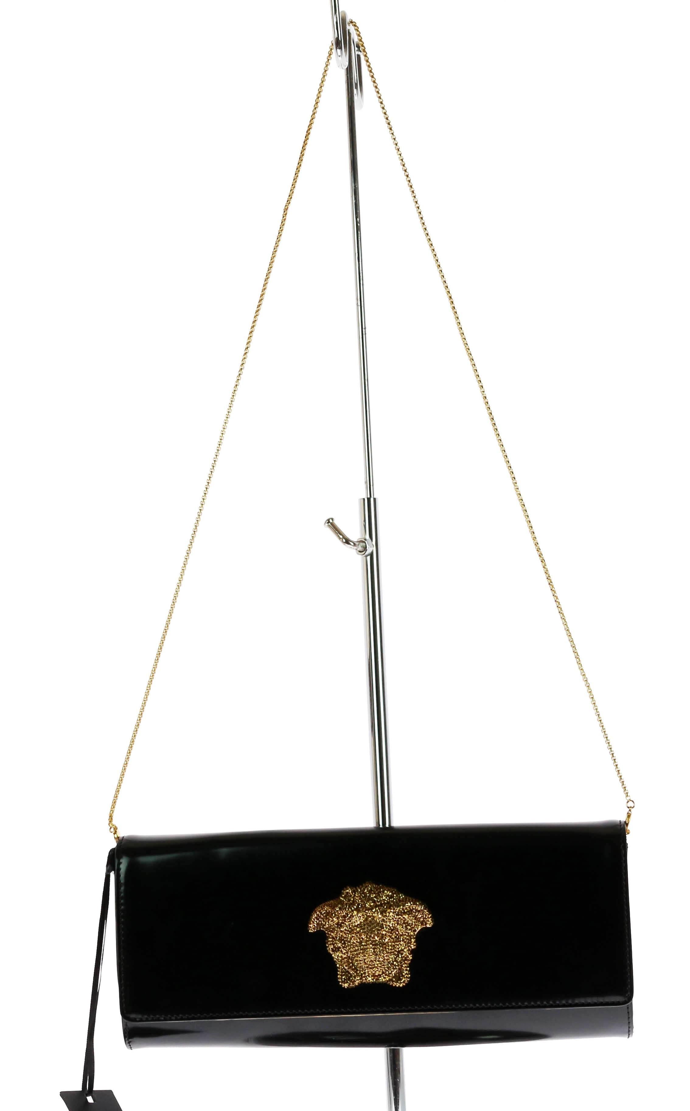 Black leather clutch from Versace featuring a foldover top with snap closure, gold-tone hardware, an internal patch pocket and an internal logo stamp.

Embellished with crystal embellished Medusa head.

New