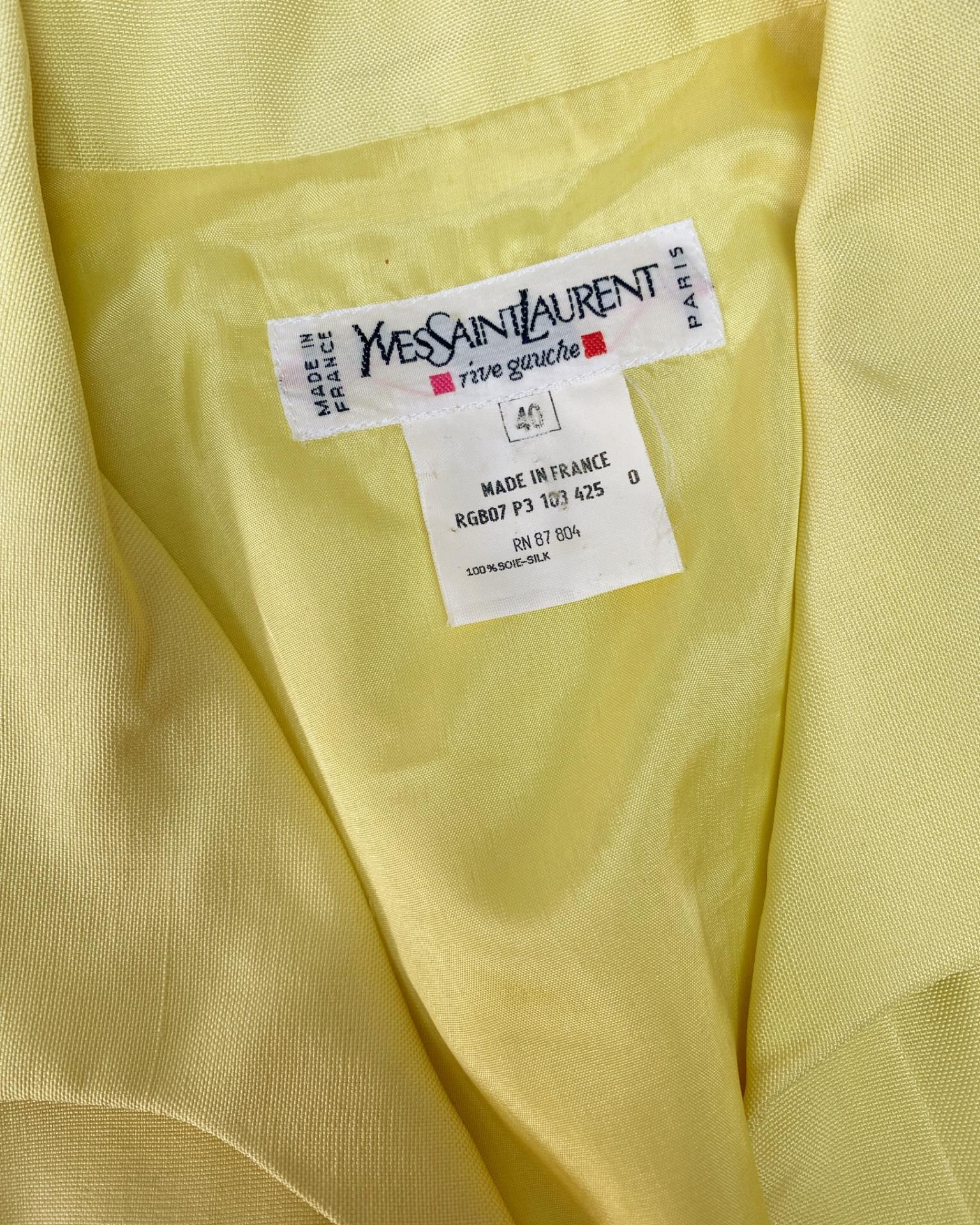 Scopri un emblema dell'audace eleganza di YSL: un abito tunica in seta vintage della fine degli anni '80, rivisitato in una tonalità giallo pallido. Traspirante, fluida e squisitamente drappeggiata, la seta 100% conferisce a questo capo una luminosa