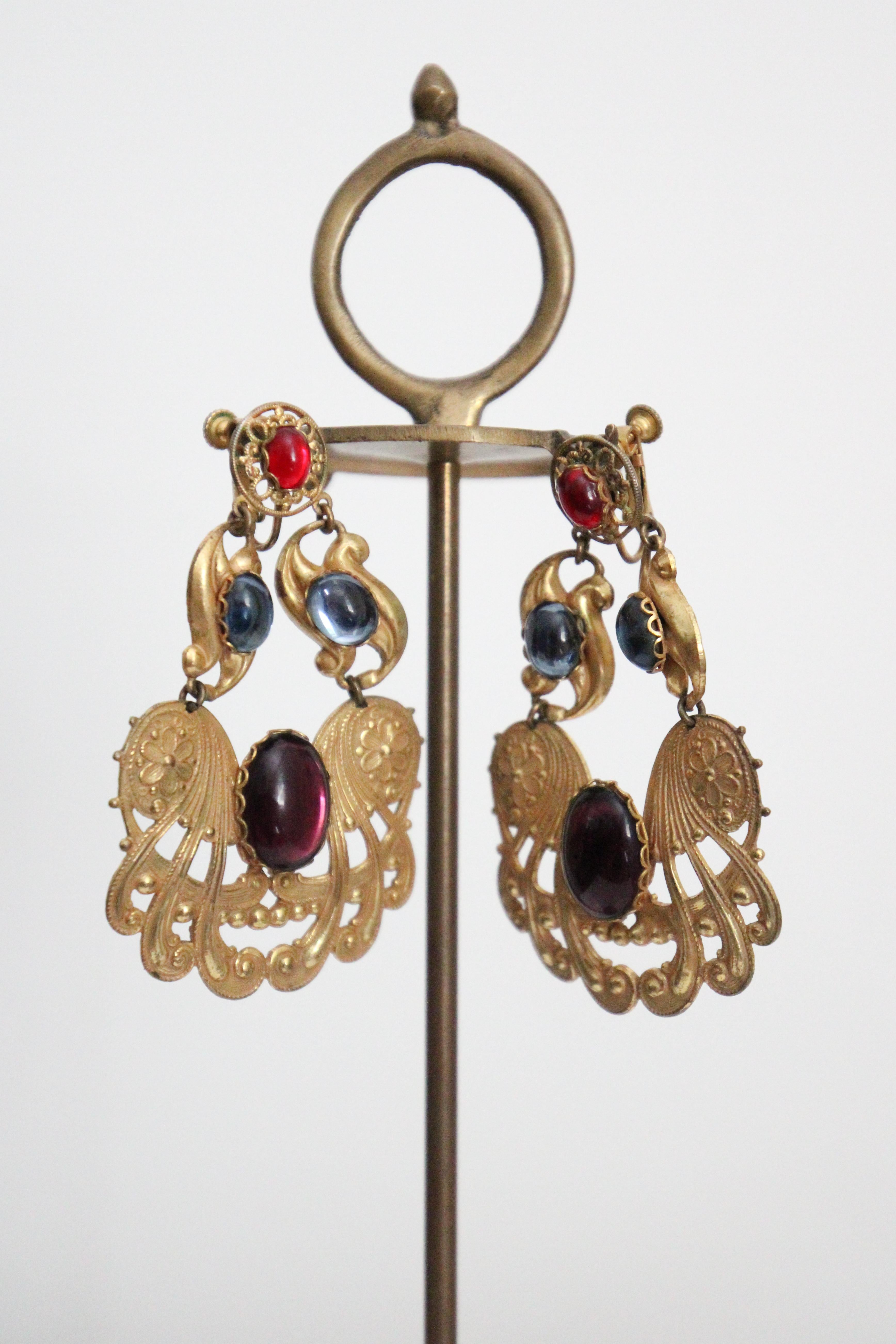 Estos espectaculares pendientes de clip de la década de 1960 de Miriam Haskell, acentuados con cabujones de cristal en tonos azul, amatista y rojo, son la pieza perfecta para añadir a tu colección de joyas vintage. 

Construidas sobre bases de
