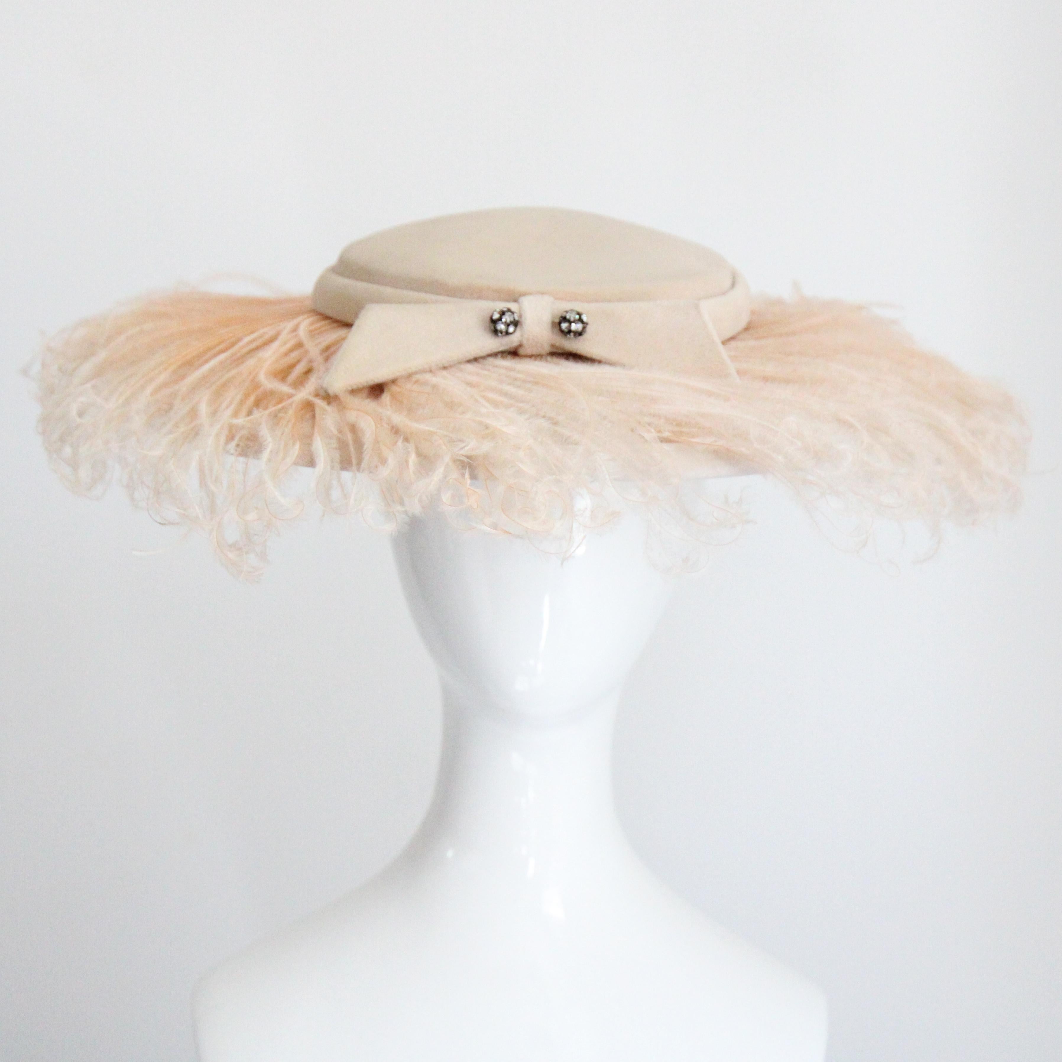 Questo magnifico cappello a piumino degli anni Cinquanta, color blush e crema, con un dettaglio di piume di struzzo lungo la tesa, è il pezzo forte perfetto per la tua collezione di cappelli. La corona modellata sul cappello è incorniciata da una