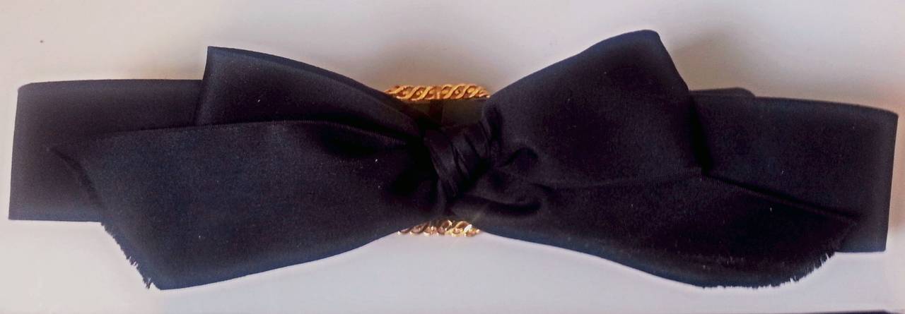 A real Chanel collector's item from Karl Lagefeld's first Autumn/Winter collection for Chanel in 1984, shortly after he was appointed head of design.

This exquisite black satin bow belt with gold buckle and detachable Camelia is utterly true to