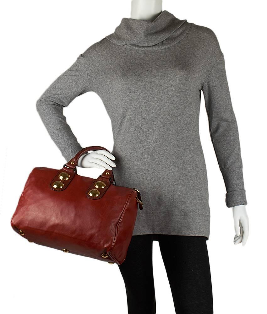 This Gucci Babouska Boston bag features a top zippered closure and two interior pockets. The large gold studs feature an engraved Gucci logo, and the gold tone hardware perfectly complements the supple red leather.