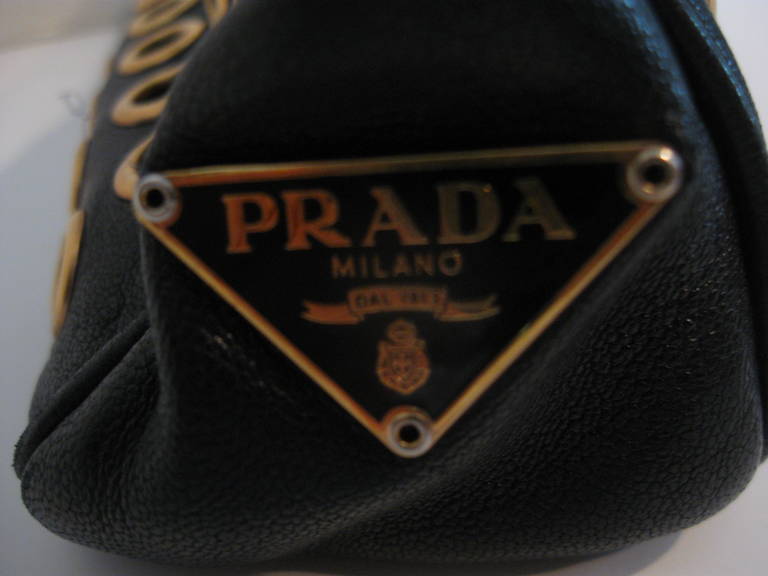 Small glove leather shoulder bag by Prada, with gold grommets.  There is a hidden magnetic snap closure, with a strap that has small gold buckles.
Interior is lined in black signature Prada fabric and has a small pocket.
Handle stands 10 inches