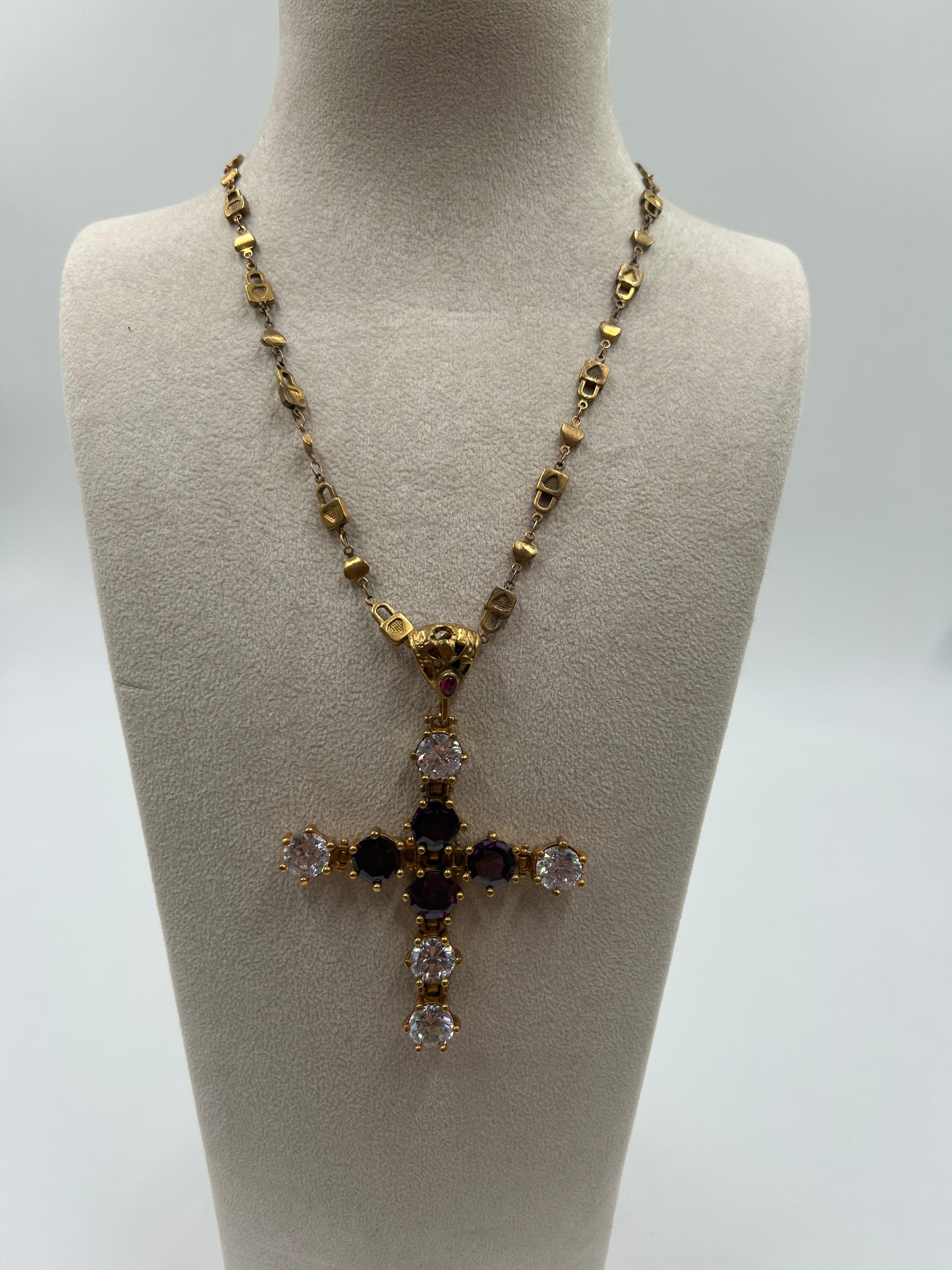 Questa collana in ottone dorato è caratterizzata da un audace ciondolo a forma di croce in smalto viola con dettagli intricati e un design di ispirazione vintage. Il ricco contrasto tra il viola intenso e la calda finitura dorata crea un look regale