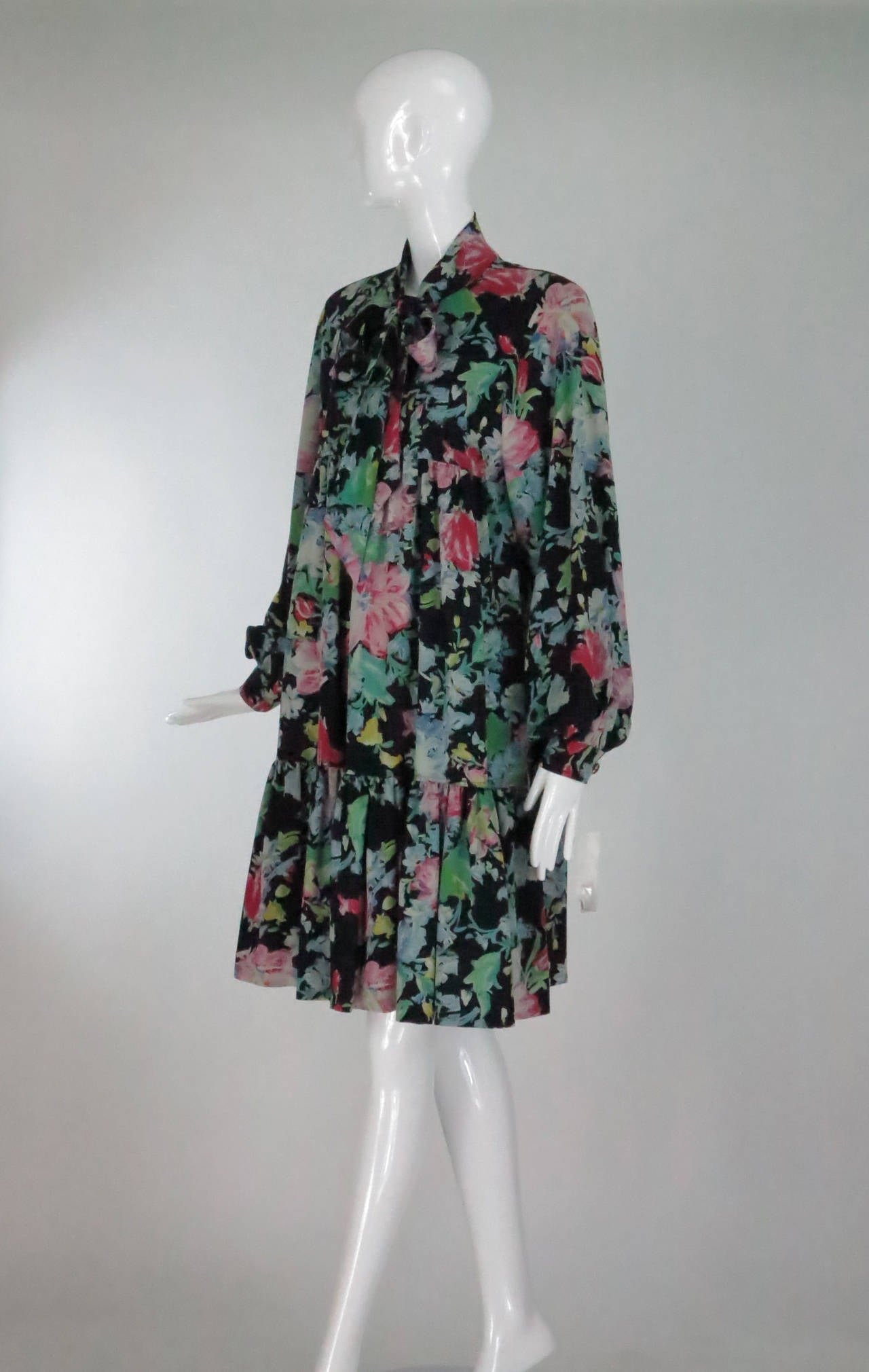 Baby doll style print dress from the late 1970s...Button front empire bodice dress is gathered below the bust and has a deep ruffle hem...Long full raglan sleeves with banded button cuffs...Attached self tie at the neck...Pull on style