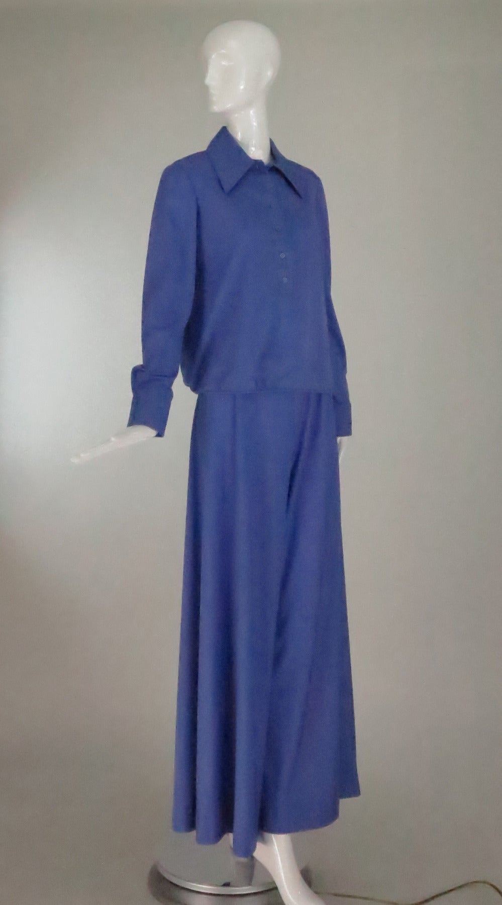 From the 1970s a silky knit two piece palazzo pant set in hyacinth blue. The pull on top has a yoke back, long sleeves with button cuffs, a button front placket and a wide collar, there is a cased drawstring at the hem. The pant sits at the natural