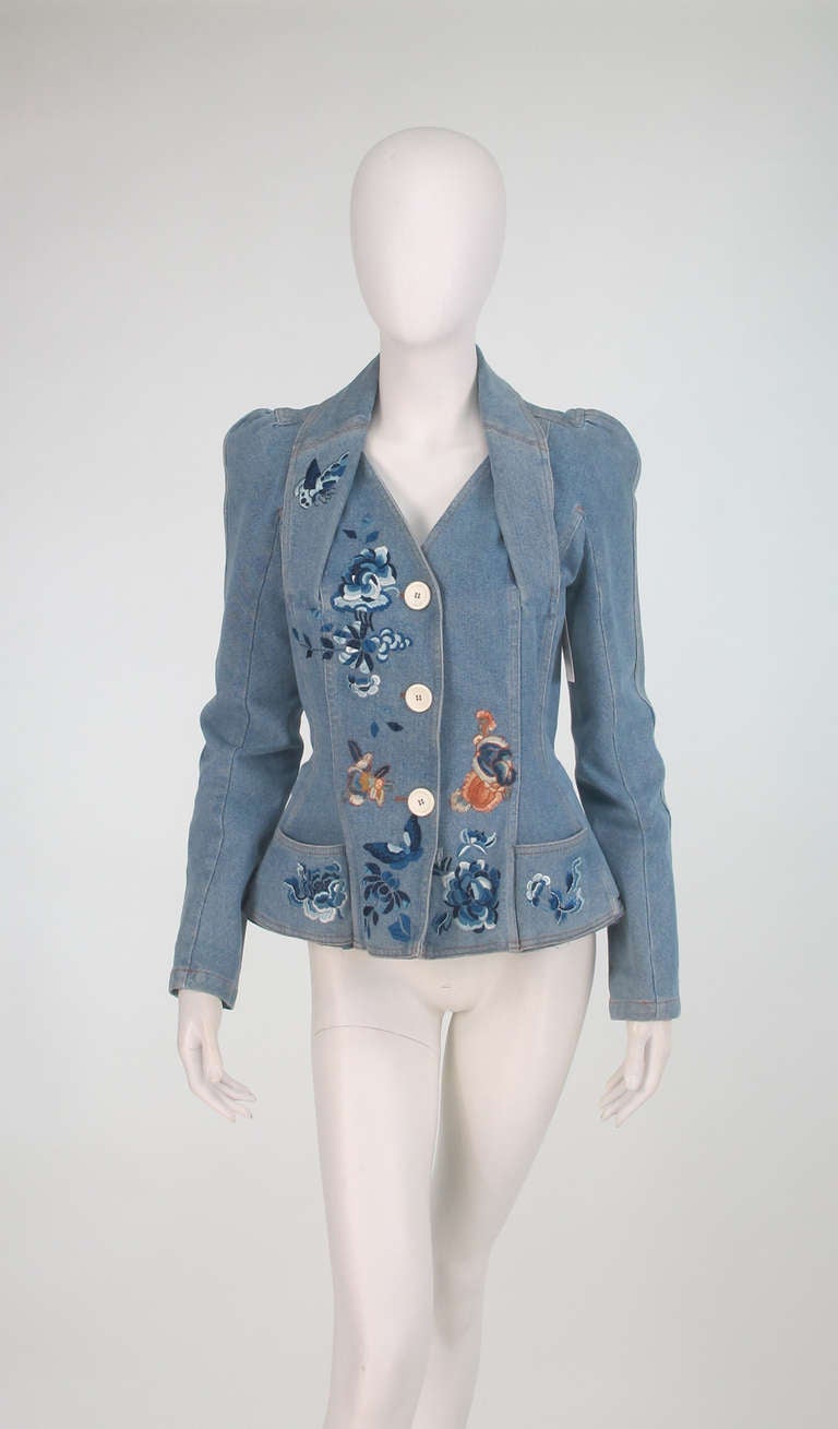 Late 1990s Dior embroidered denim jacket...Medium weight distressed denim in light blue...Victorian inspired with peaked shoulders, fitted waist and little hip front pockets and padded hip peplum...Embroidered with butterflies and flowers...Closes