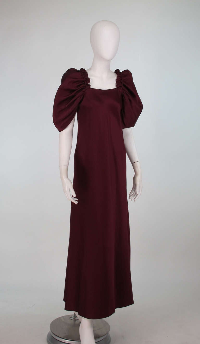 1960s Stavropoulos garnet silk renaissance inspired evening gown...Mid weight silk satin gown in garnet red...The draped peaked sleeves have self cords at each shoulder top front bodice front to back...The dress is a narrow A line shape at front,