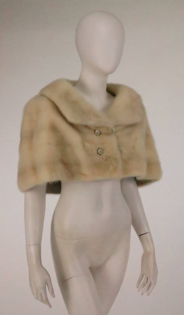 Creamy white mink cropped capelet from the 1950s...Shawl collar...Closes at the front with loops and white rhinestone buttons...Fully lined in silk...In lovely condition, it would be perfect for a winter wedding!

Measurements are:
Shoulder line