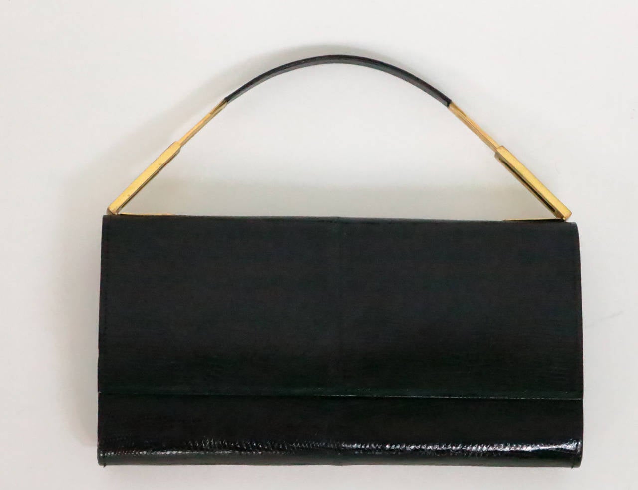 Glazed black lizard handbag/clutch from the 1970s…Flap closure bag has gold plated hardware and a retractable lizard handle, the bag is rounded at the bottom…Center flap snap closure…The interior is lined in tan suede with a single zipper
