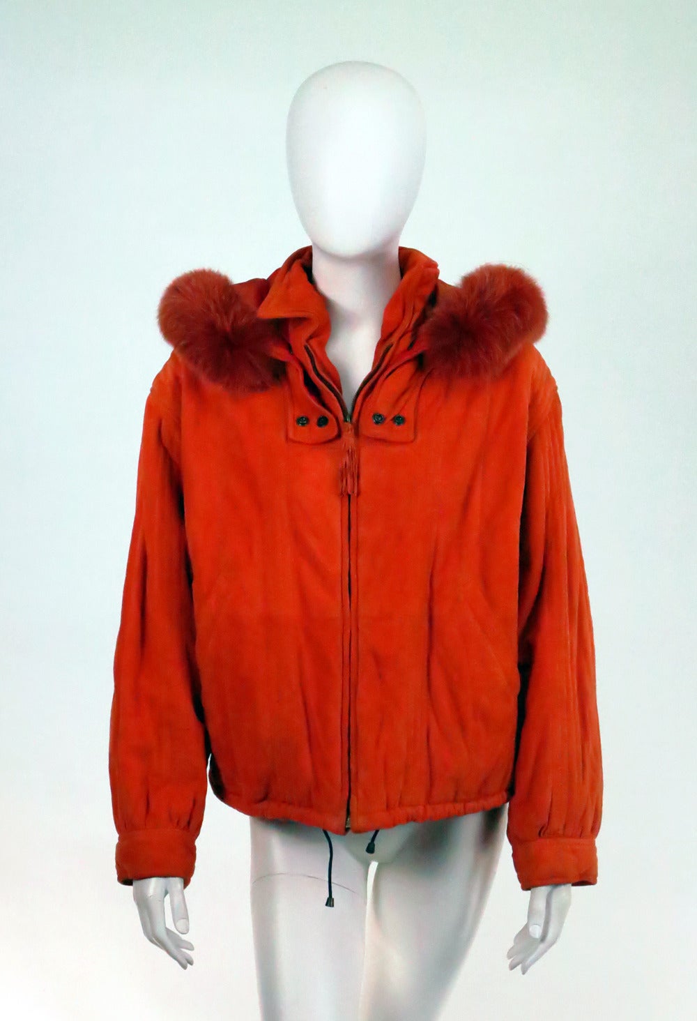Buttery soft suede in Persimmon with a removable hood trimmed in dyed fox...From the 1970s...Made by Oggi, Italy...The jacket closes at the front with a tasseled zipper...Vertical quilt stitch details...There are angled, banded front pockets...The