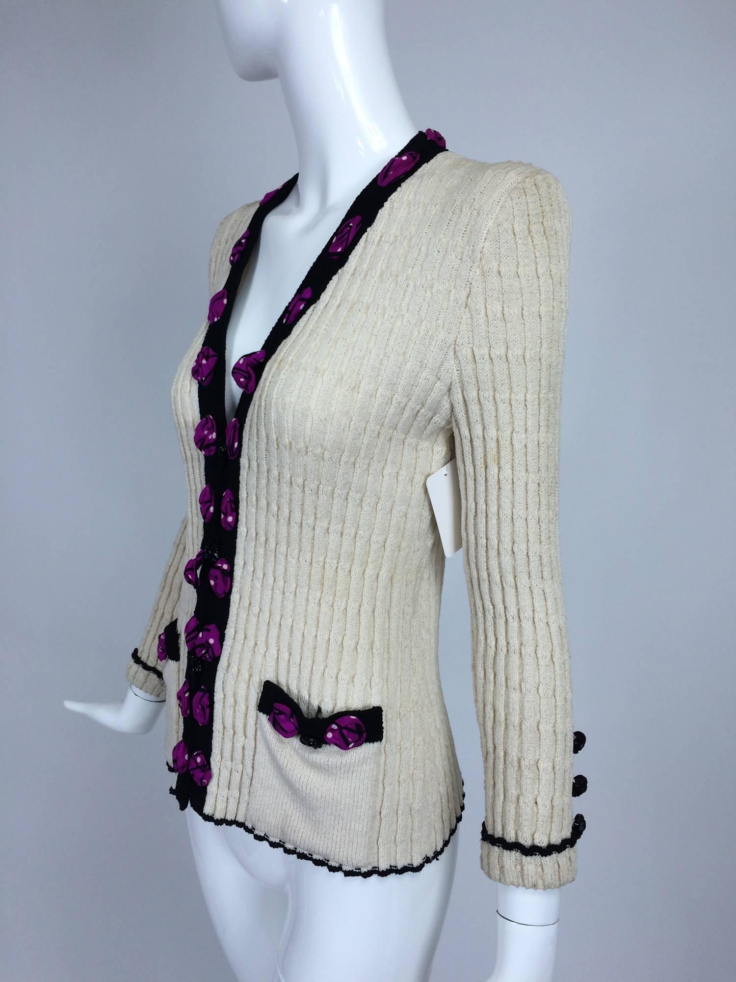 Adolfo cream cable knit rosette trimmed cardigan sweater/jacket 1970s...Fitted cable knit V front sweater is trimmed in black knit and has appliqued silk fabric rosettes on the front facings and pockets...Closes with black glass buttons, there are
