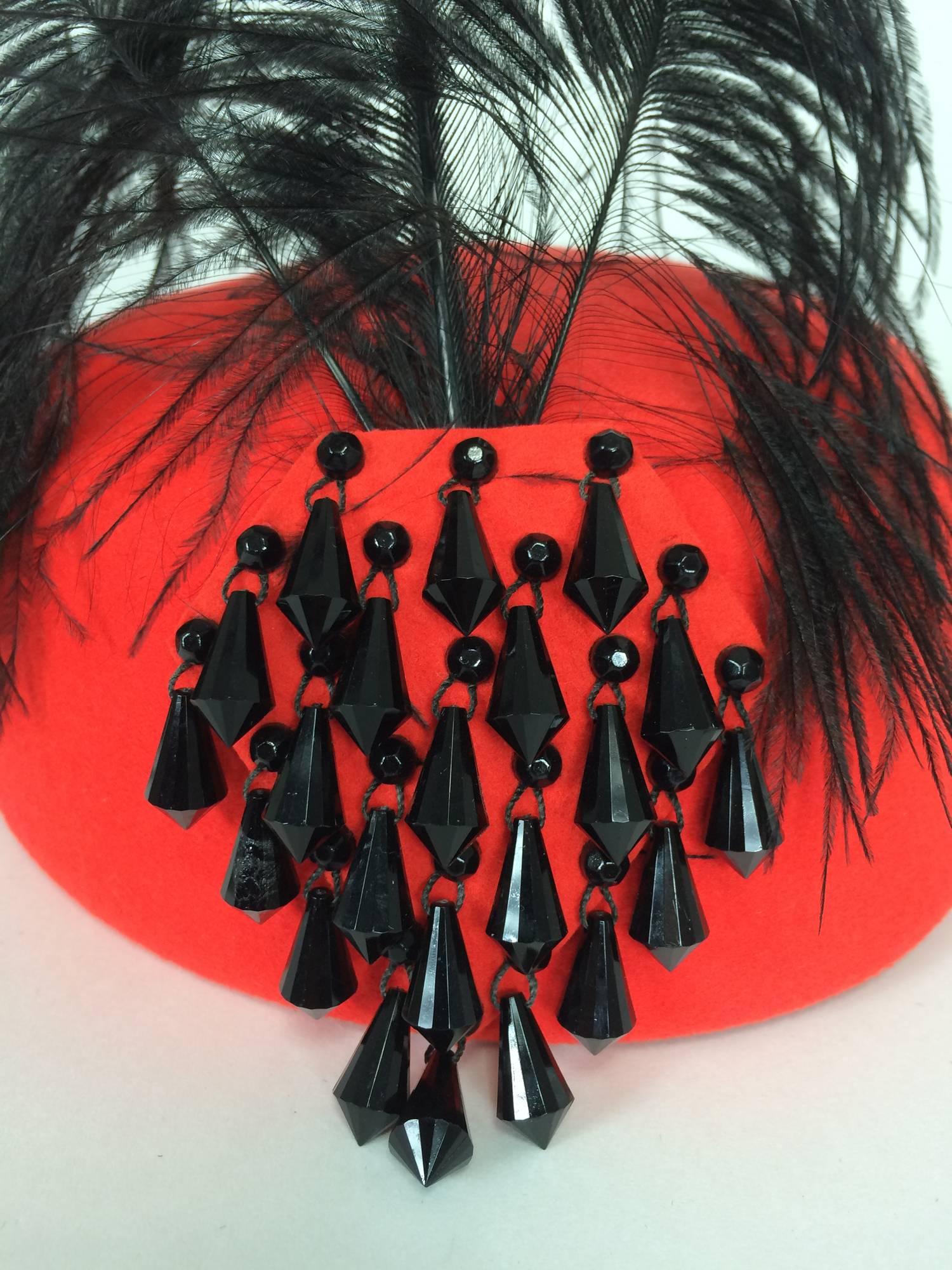 Halston beaded and feathered coral red hat 1970s...Coral red wool hat in a classic style the front features a panel of black faceted tear drops in black, above is a cockade of black bird of paradise feathers...There are combs at either inside to