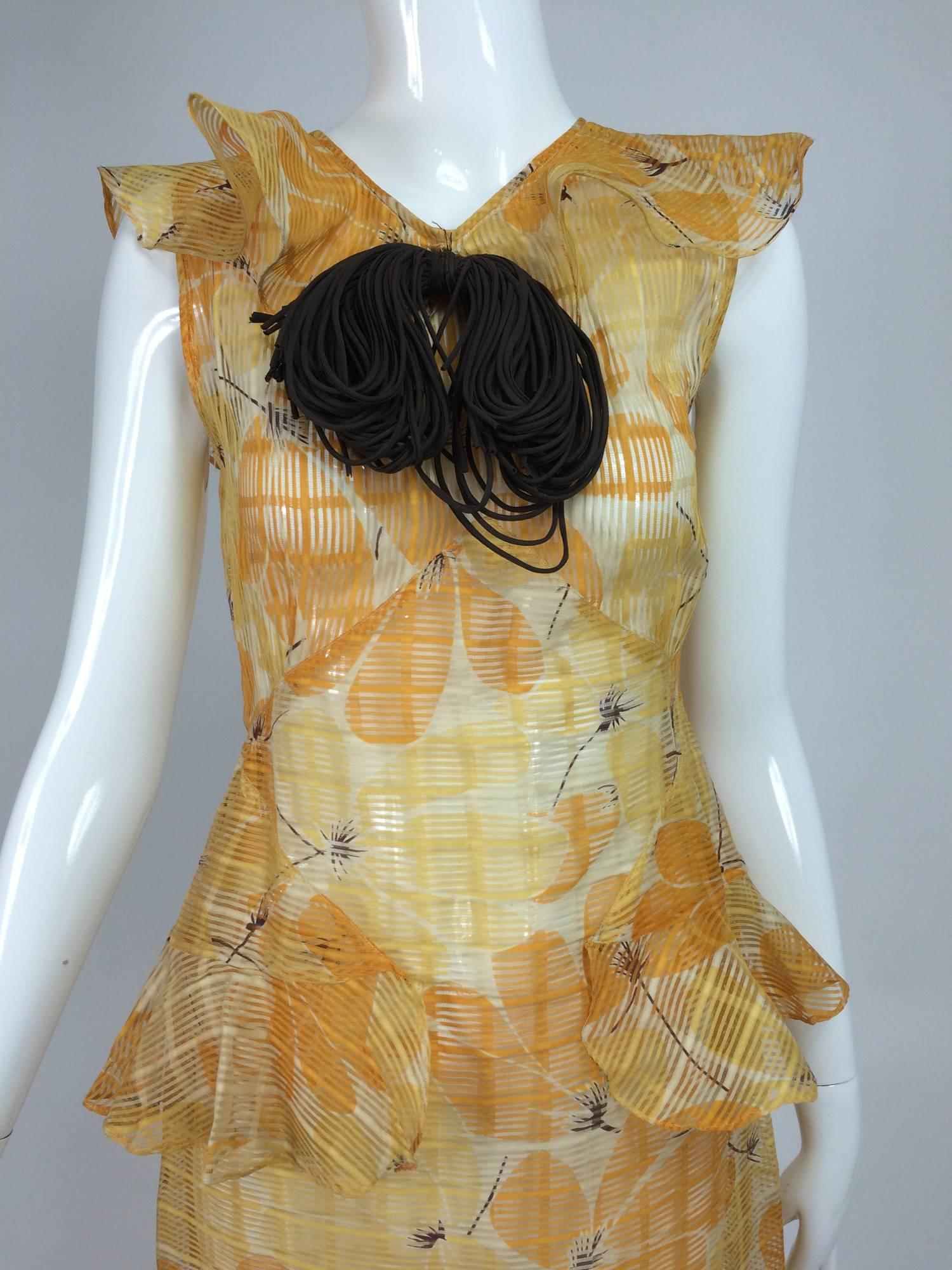 Unworn, sheer woven (in a grid pattern) organdy dress from the 1930s, in a very modern, for the time, print of tonal orange flowers that have brown stems and centers, set against a cream ground...The sleeveless dress has a ruffle at the front that