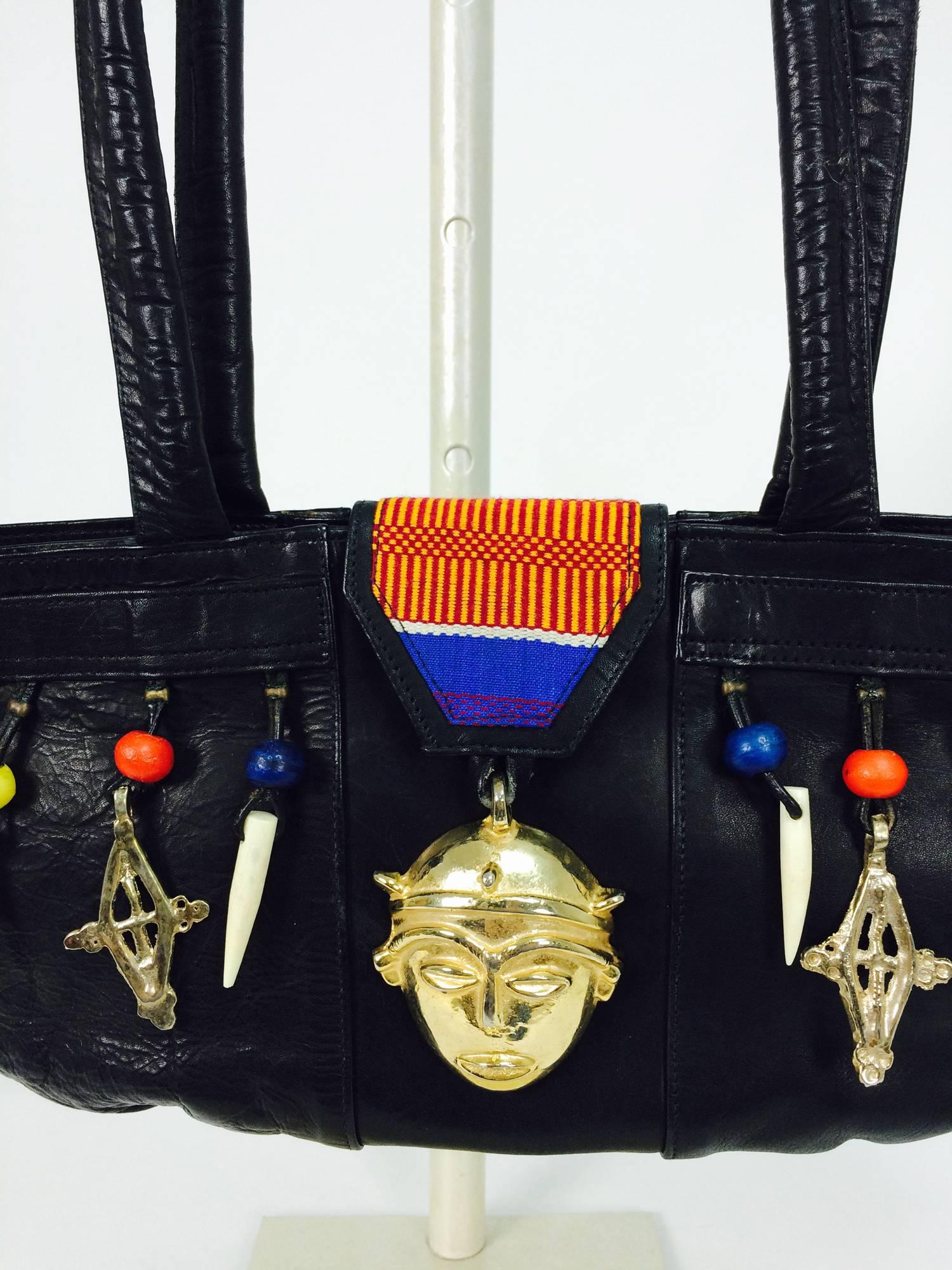 Novelty black leather tribal charm unique shape handbag...Black leather shoulder handbag with an exaggerated shape bag & shoulder straps...The front of the bag is decorated with gold metal charms, wooden beads and bone tusks...A coloured woven