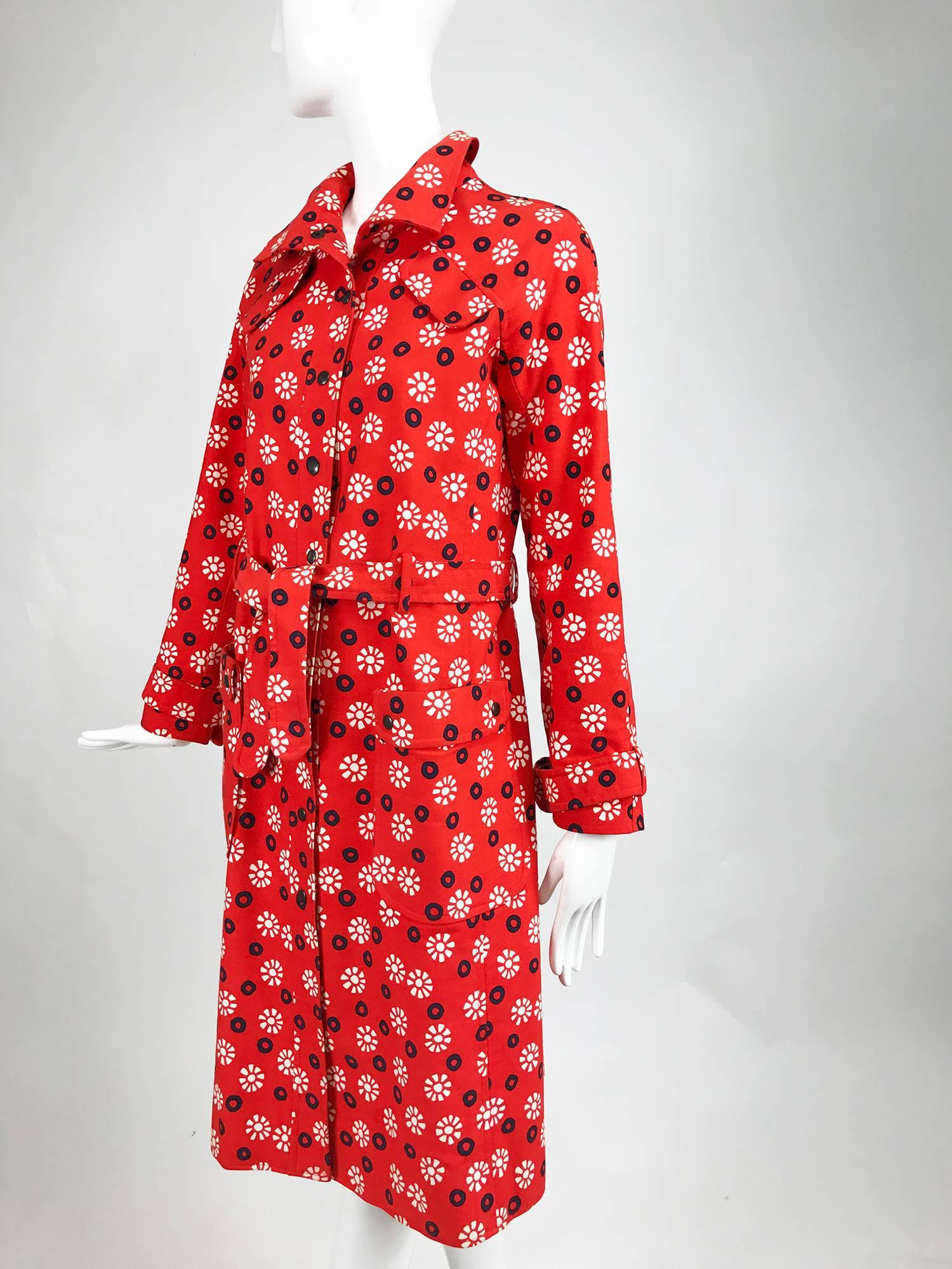 Ungaro Parallele red, white and navy blue with black center circles with white floral printed red cotton canvas trench coat from the late 1960s. Black snap front coat has a self tie belt, shoulder flaps at the front, 2 hip front patch pockets with