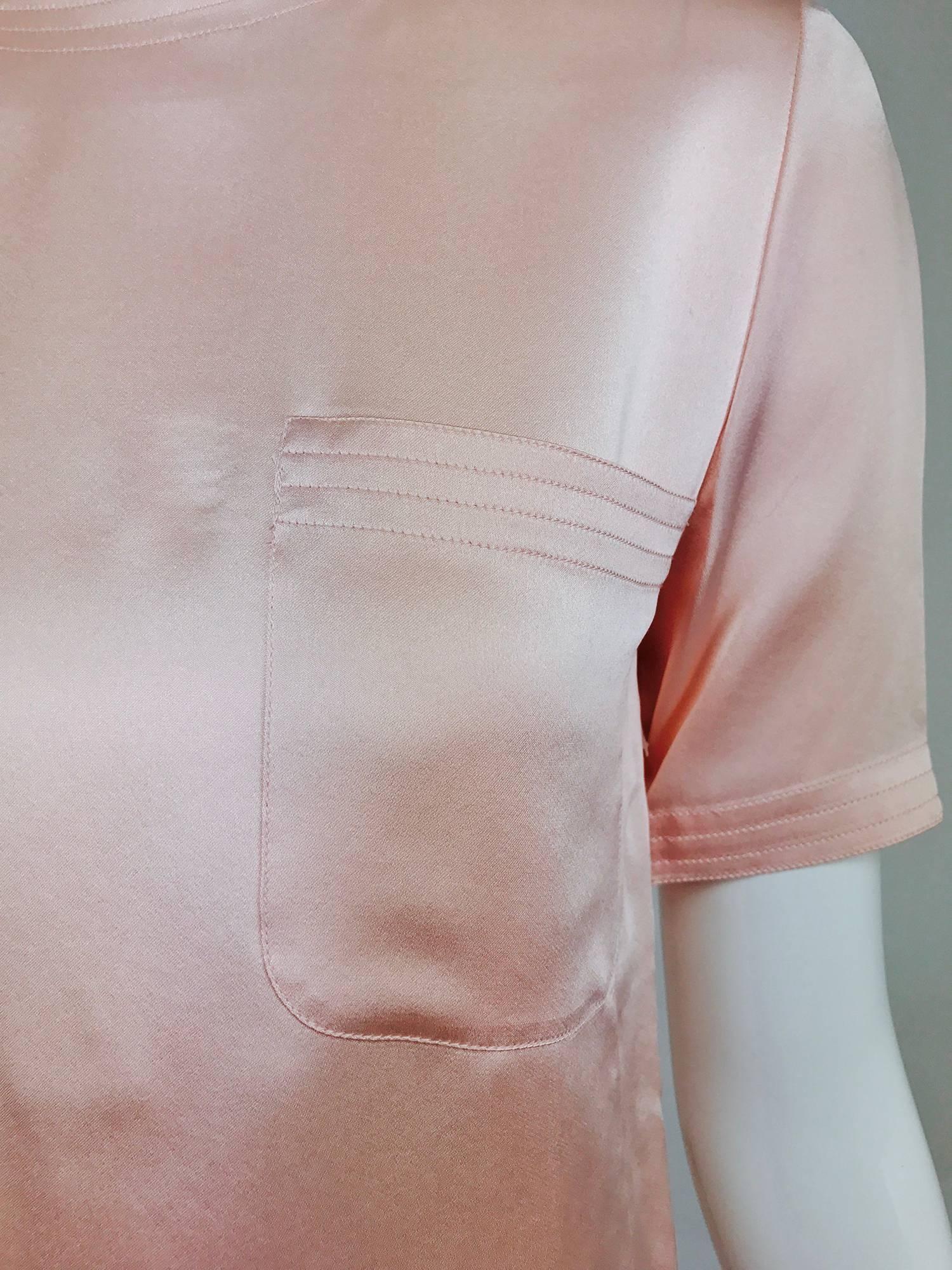 Classic Chanel short sleeve suit blouse in pale pink silk satin from the 1970s...The blouse has three rows of top stitching detail at the neckline, sleeve edges and hem...Single open breast pocket...Closes at the neck back with 5 signed gold Chanel