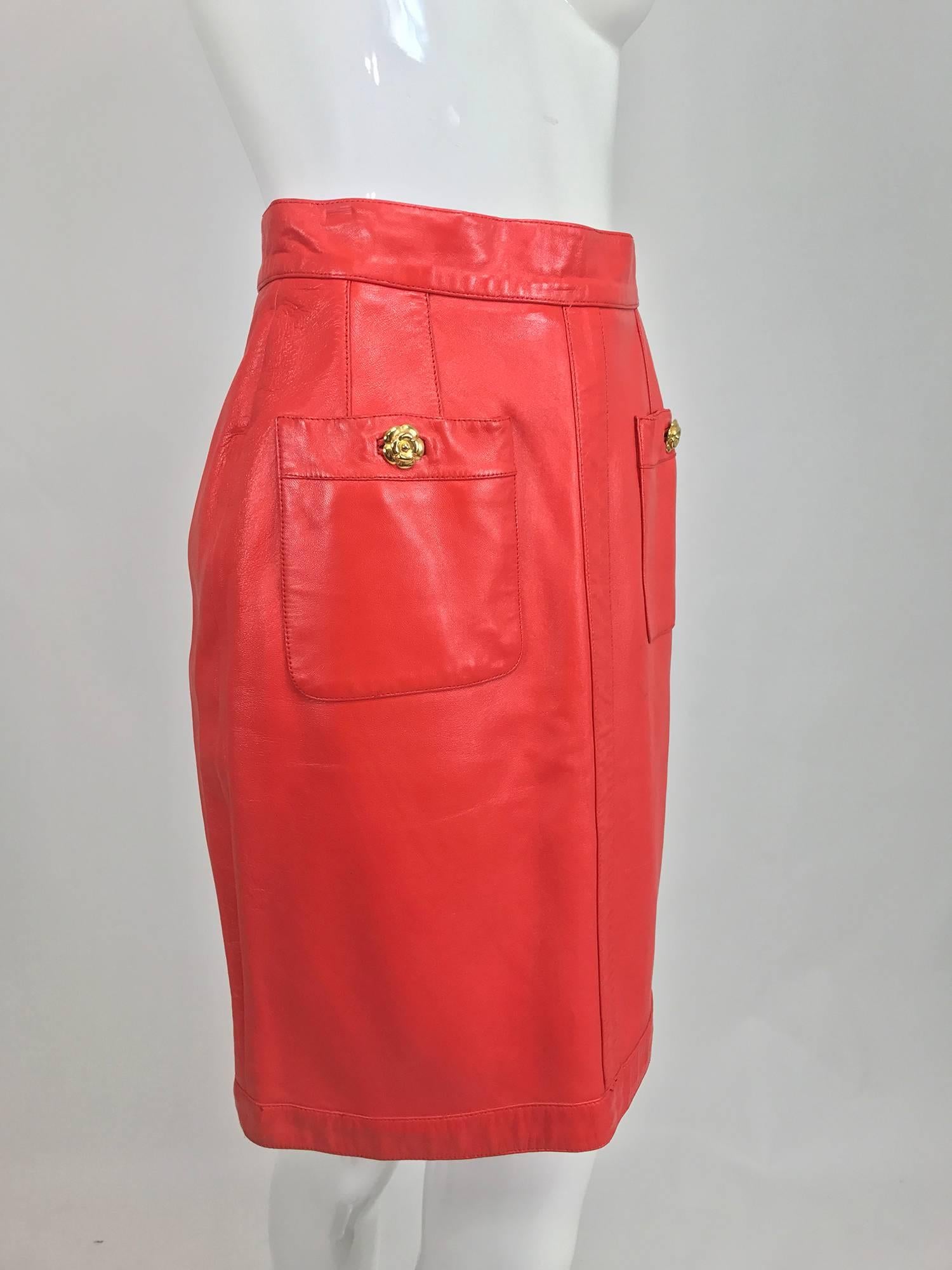 Chanel Vintage 1990s coral red leather skirt with pockets...Soft leather skirt sits at the natural waist, is fitted through the hip and falls straight to the hem...Two hip front patch pockets close with gold Chanel camellia flower buttons, lots of