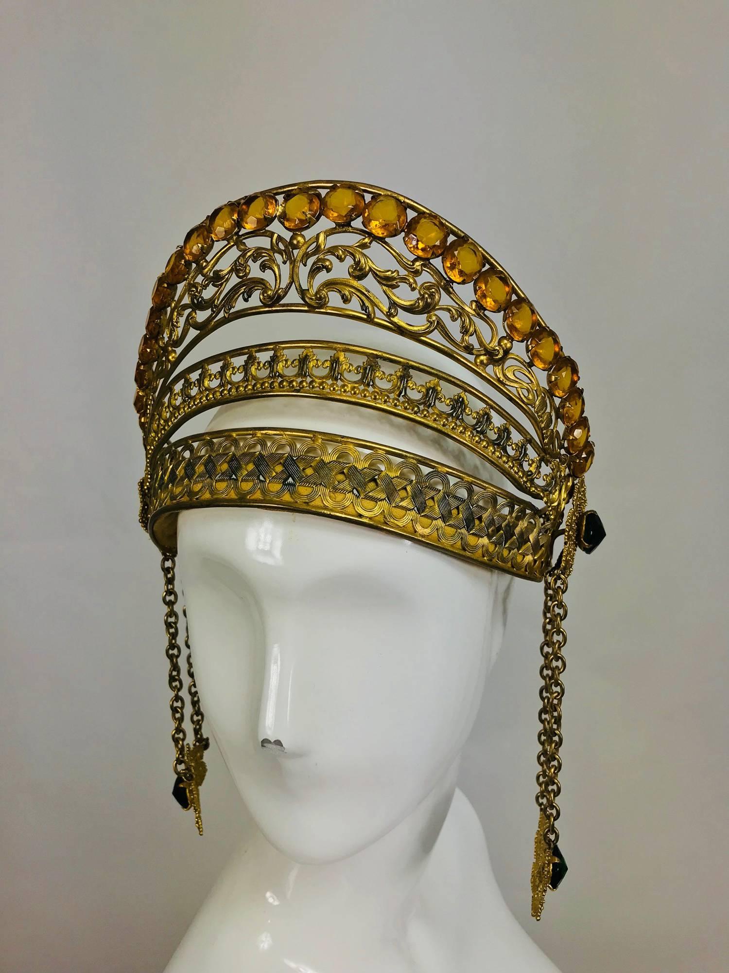 Rare Crown or headdress from the early 1900s, constructed of embossed, cut out and woven gilt metal, the top is set with amber cut faceted jewels...At each side are gold filigree disks set with faceted green stones, hung below are chains, the