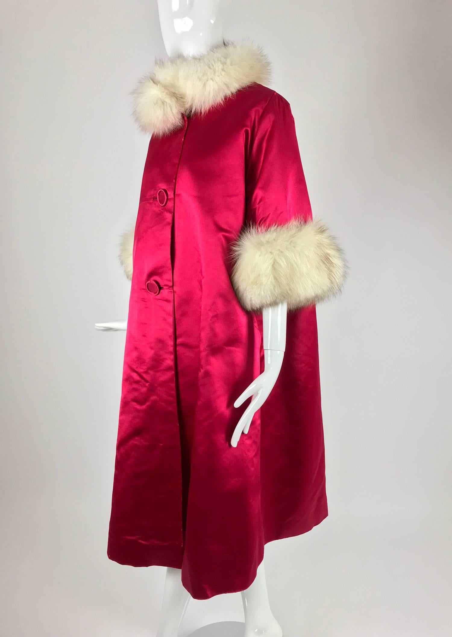 Vintage red silk slipper satin fur trimmed evening coat from the 1960s. Tent shape evening coat that flares at the hem. Off white fox fur collar. Bracelet length sleeves are trimmed in deep off white fox fur cuffs. The coat closes at the front with