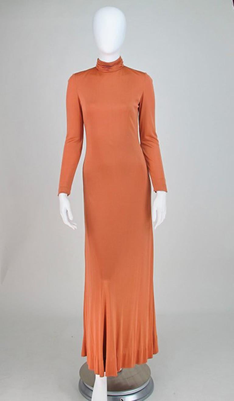 Christian Dior New York silk jersey maxi dress from the 1970s. Sleek, fine pale pumpkin silk knit gown, with ruched high neck, long tapered sleeves with a single snap closure at each wrist. The dress is fitted through the torso, to the hip and