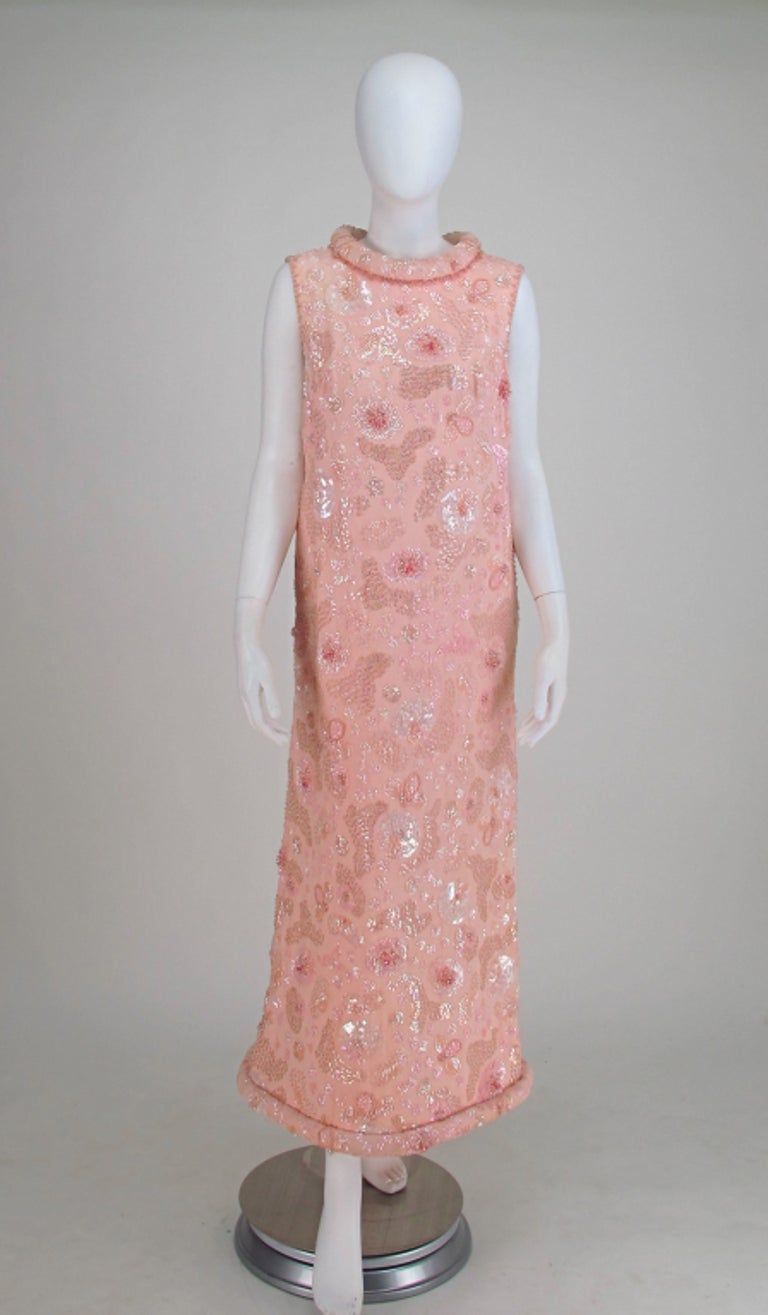 Bonwit Teller candy pink beaded sequin silk chiffon, roll hem evening dress from the early 1960s. This beautiful dress is a gorgeous example of early 1960s evening glamour. The sleeveless dress features a stand away rolled and padded neckline and