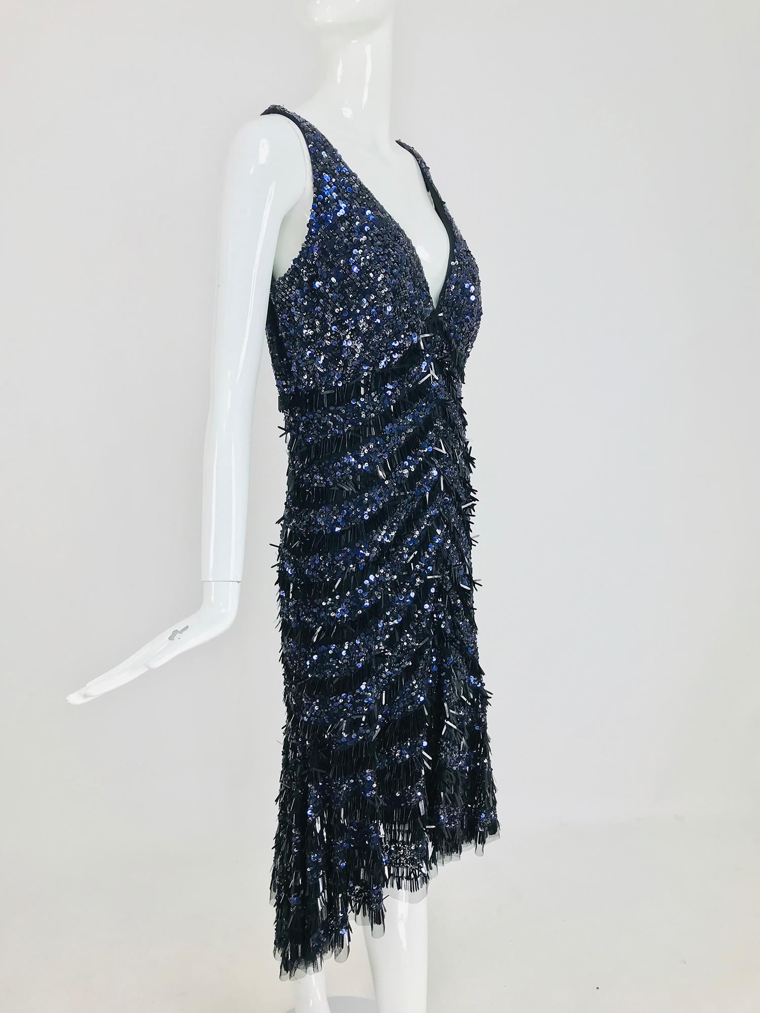 Theia sequin cocktail evening dress in black and blue. Beautiful glittery shaped sequins cover this entrance making dress. Sleeveless V neckline dress skims the body and flares to the hem which is trimmed in black tulle.  The dress dips slightly at