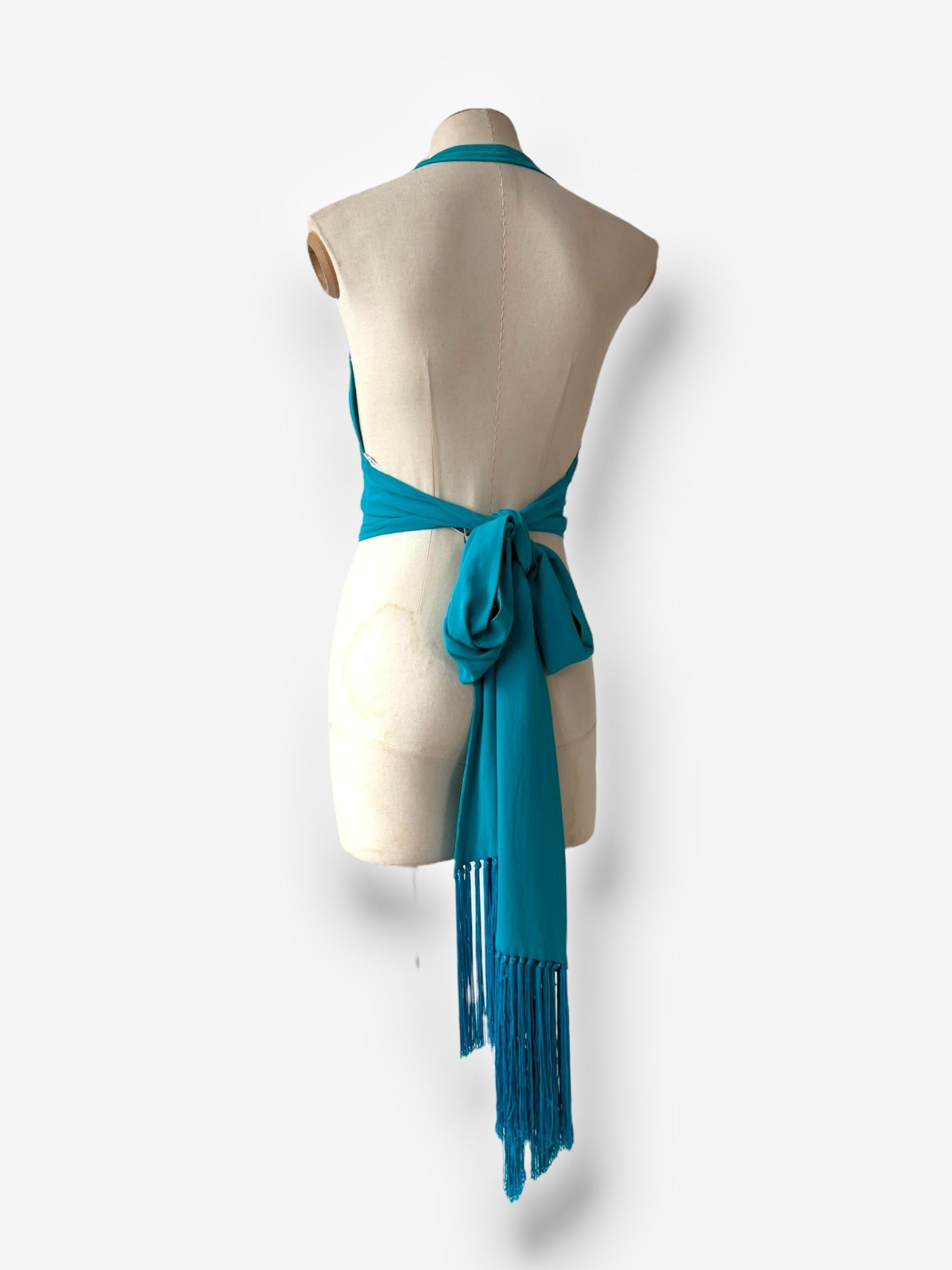 
Exemple frappant du bohémianisme raffiné de Céline, ce haut de style enveloppant est confectionné en soie turquoise vibrante et rehaussé de subtils détails en forme de houppes. Sa construction fluide et ajustable lui permet d'envelopper
