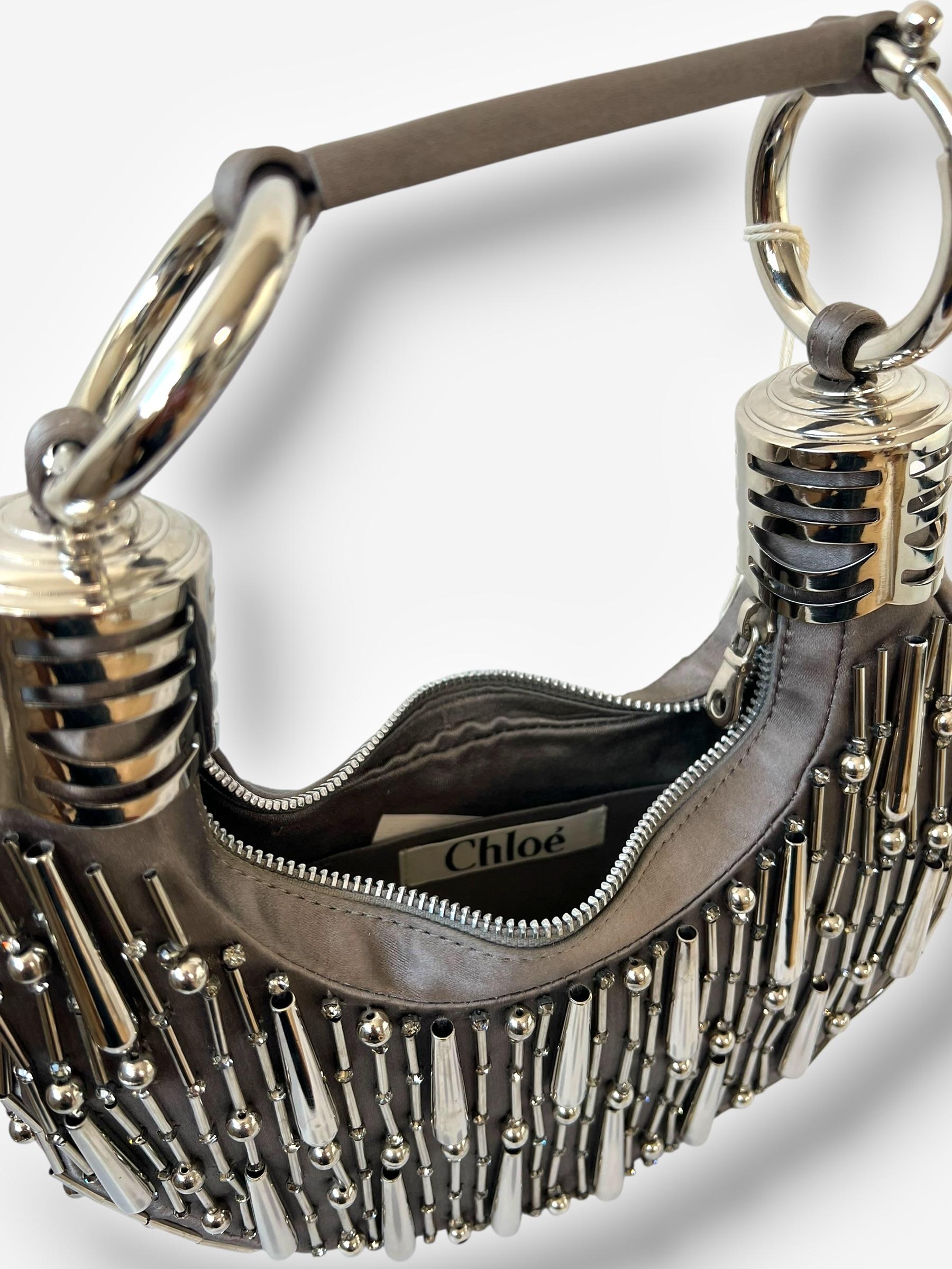 
Esempio di accessori da sera dei primi anni 2000, questa borsa bracciale della collezione Collection'S 2005 di Chloé è realizzata in raso color tortora e impreziosita da perline e strass argentati. Un'elegante chiusura con zip si apre su un interno