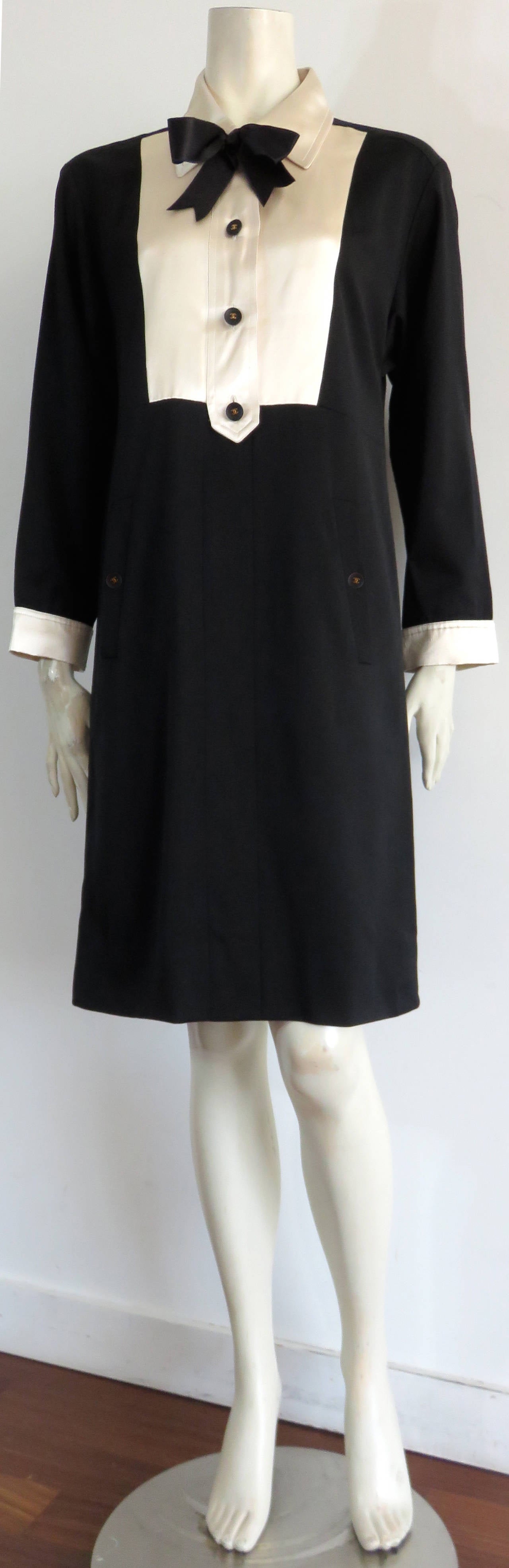 Lovely CHANEL PARIS Silk, bib-front, 'tuxedo' dress.

Black wool shell with ivory silk bib front, collar, and cuffs.  Silk, black ribbon bow  detail at front neck.  

Black buttons with gold finished, metal 'CC' logo centers.

Twin front