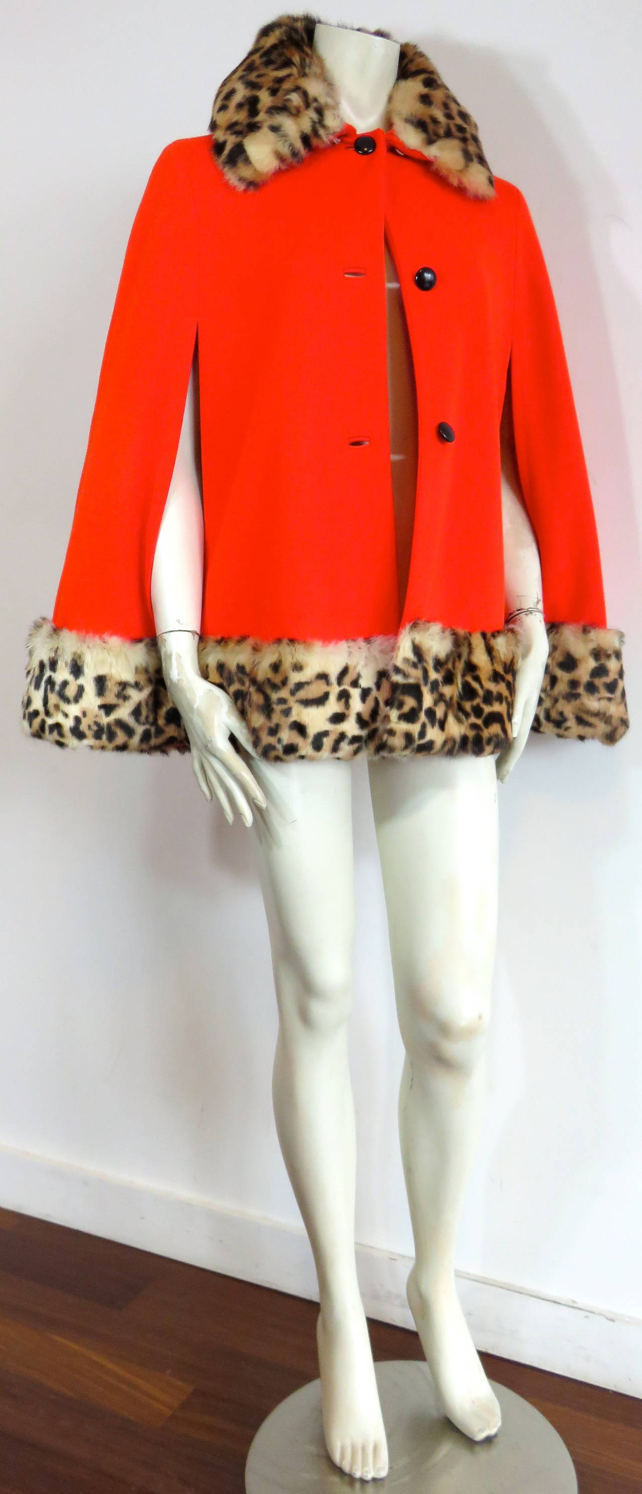 Stunning, 1960's LILLI ANN Fur trimmed, wool knit cape.

Thick, dark tangerine, red-tone wool knit jersey shell with ultra-soft, leopard printed, rabbit-fur collar, and hem trimming.

Long arm slits at front with smooth, black leather-faced dome